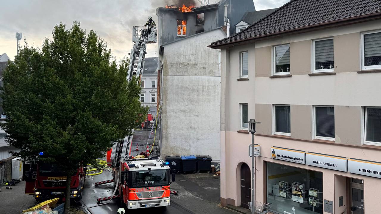 Flammen schlagen aus dem Dach eines mehrstöckigen Hauses, die Feuerwehr hat die Drehleiter ausgefahren.