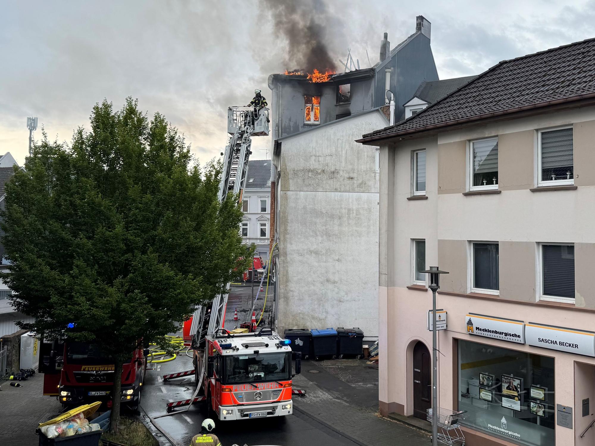Flammen schlagen aus dem Dach eines mehrstöckigen Hauses, die Feuerwehr hat die Drehleiter ausgefahren.