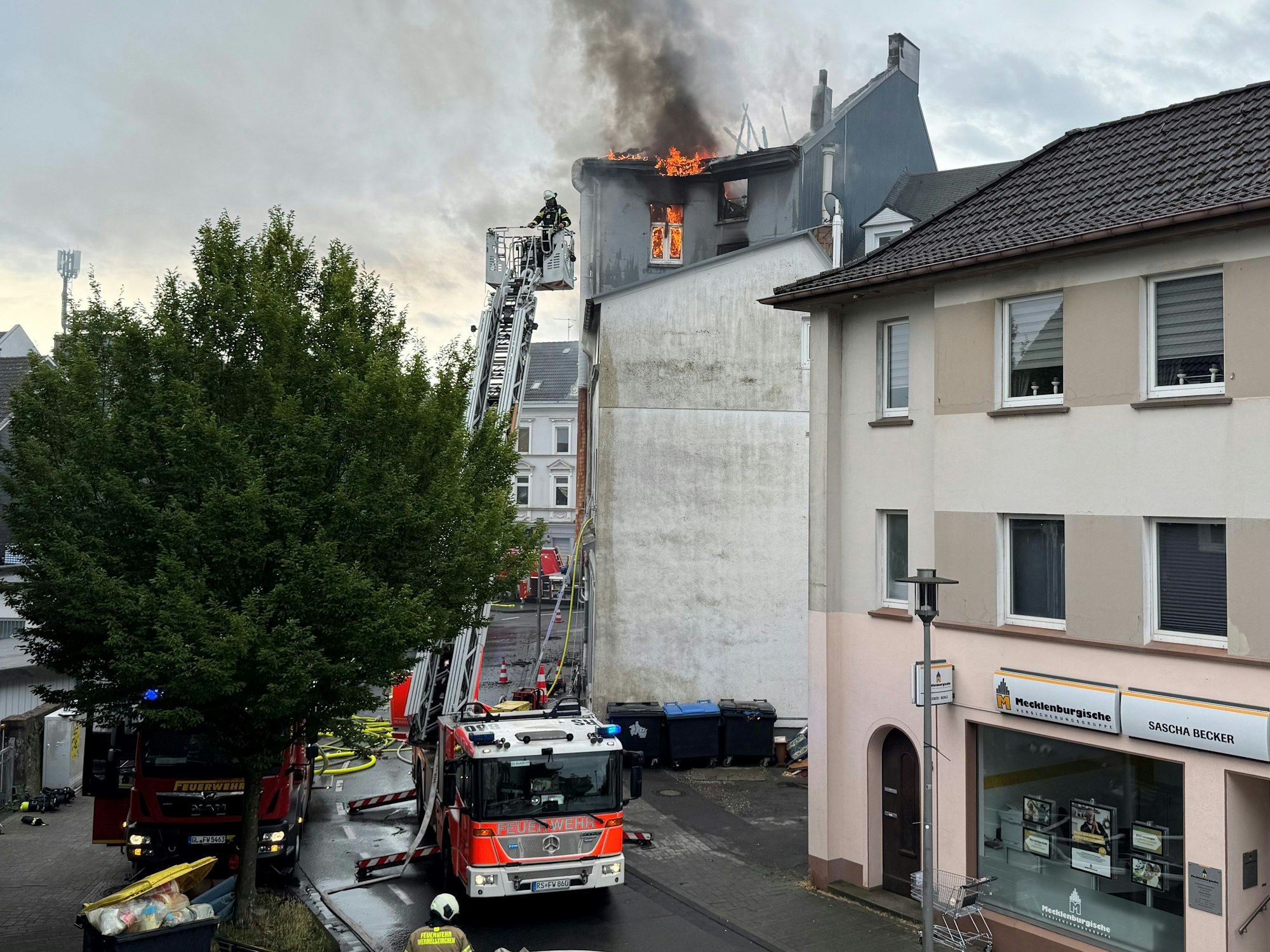 Flammen schlagen aus dem Dach eines mehrstöckigen Hauses, die Feuerwehr hat die Drehleiter ausgefahren.