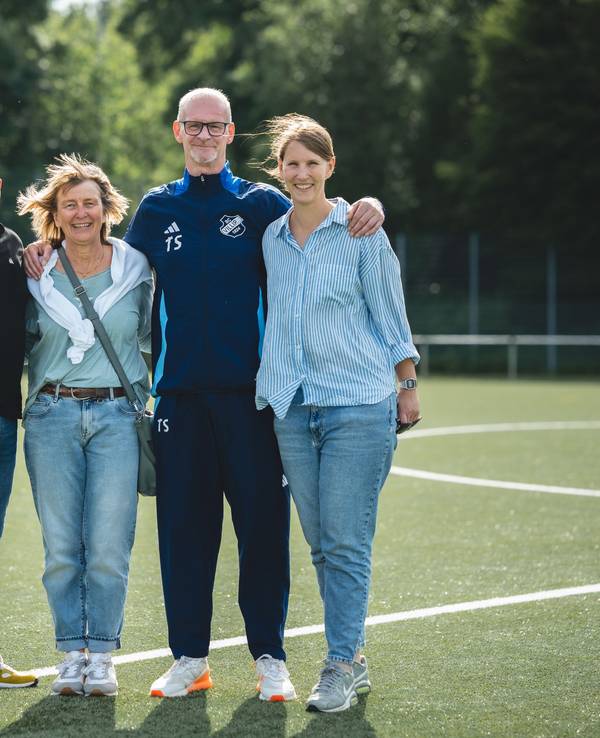 Ein Mann hat seine Arme um die Schultern zweier Frauen gelegt, daneben steht ein weiterer Mann.