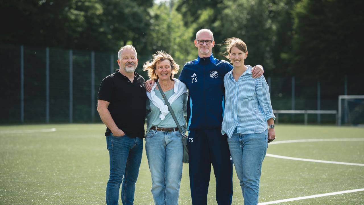Ein Mann hat seine Arme um die Schultern zweier Frauen gelegt, daneben steht ein weiterer Mann.