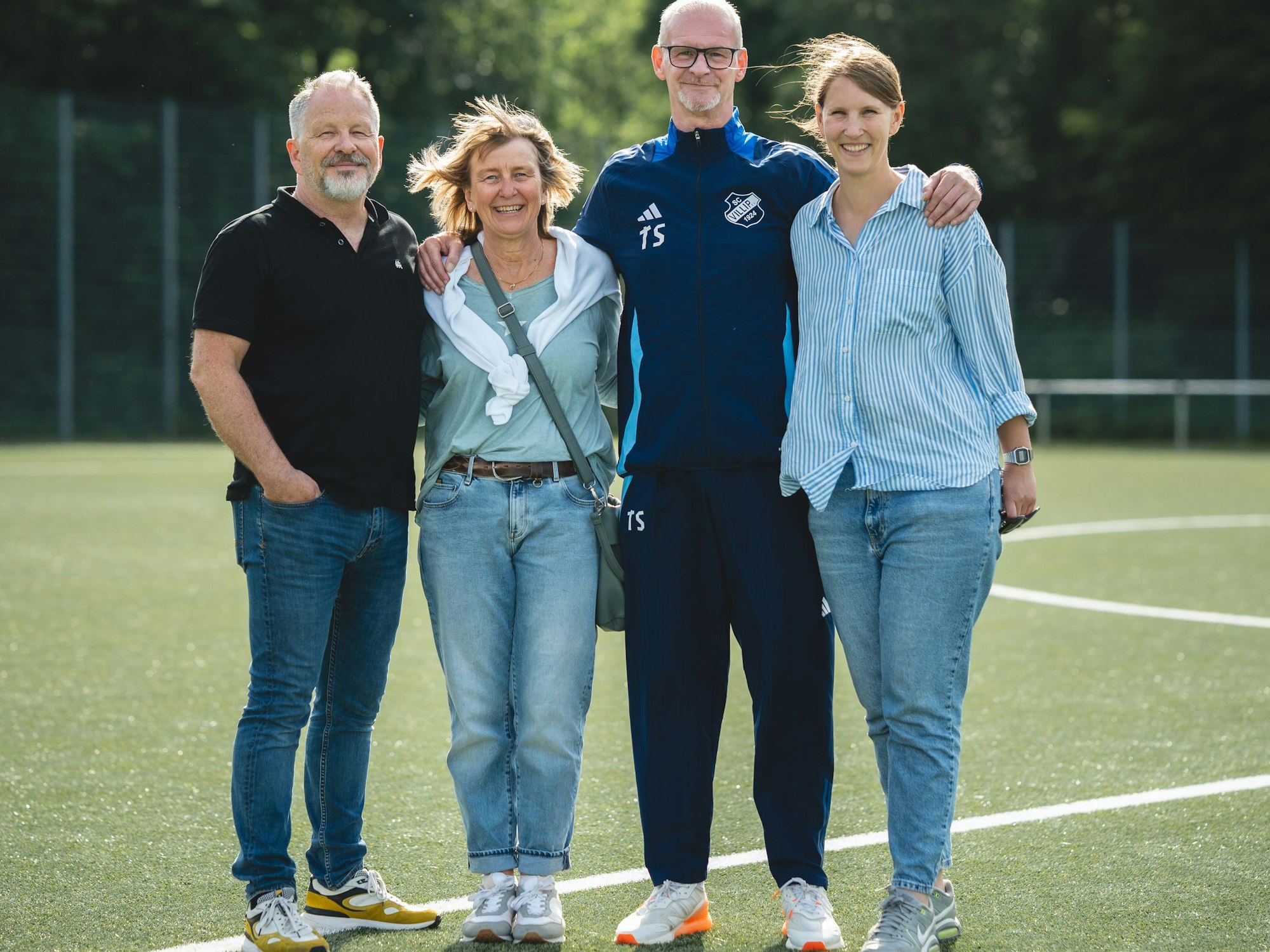 Ein Mann hat seine Arme um die Schultern zweier Frauen gelegt, daneben steht ein weiterer Mann.