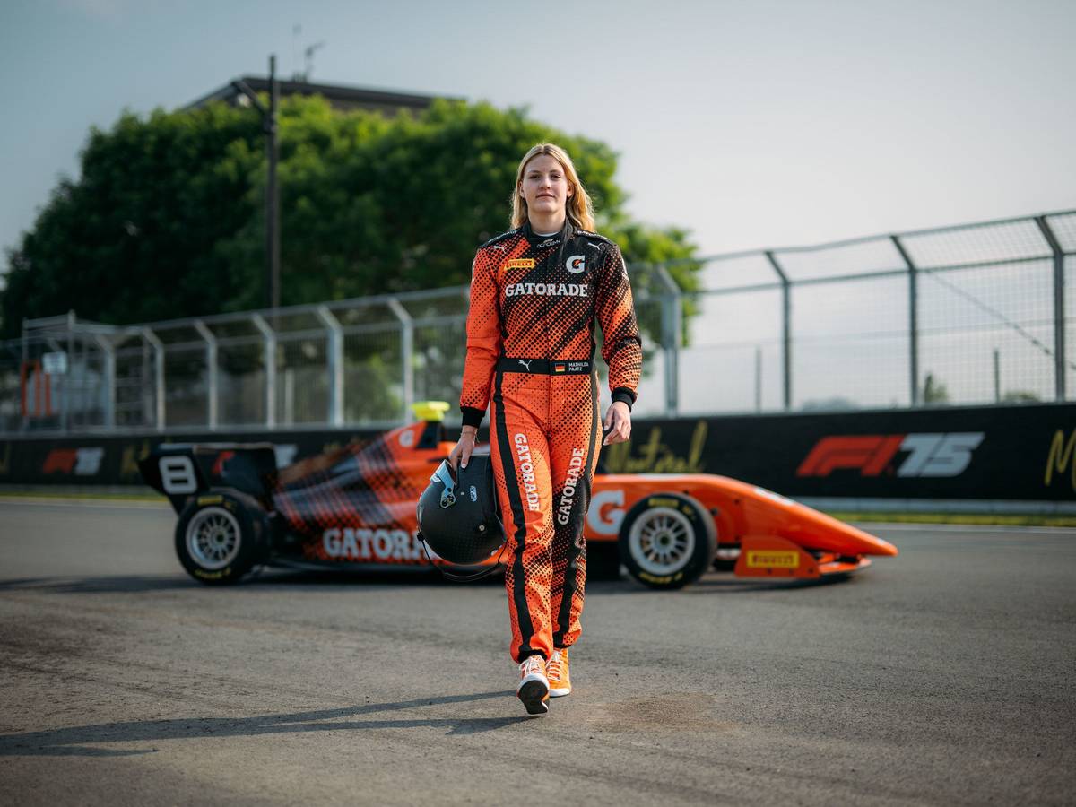 Mathilda Paatz vor ihrem Rennauto in orangener Fahrkleidung.