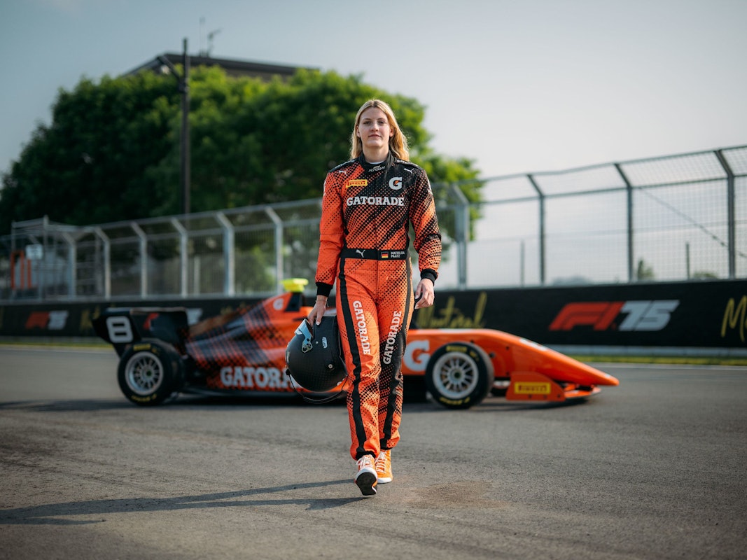 Mathilda Paatz vor ihrem Rennauto in orangener Fahrkleidung.