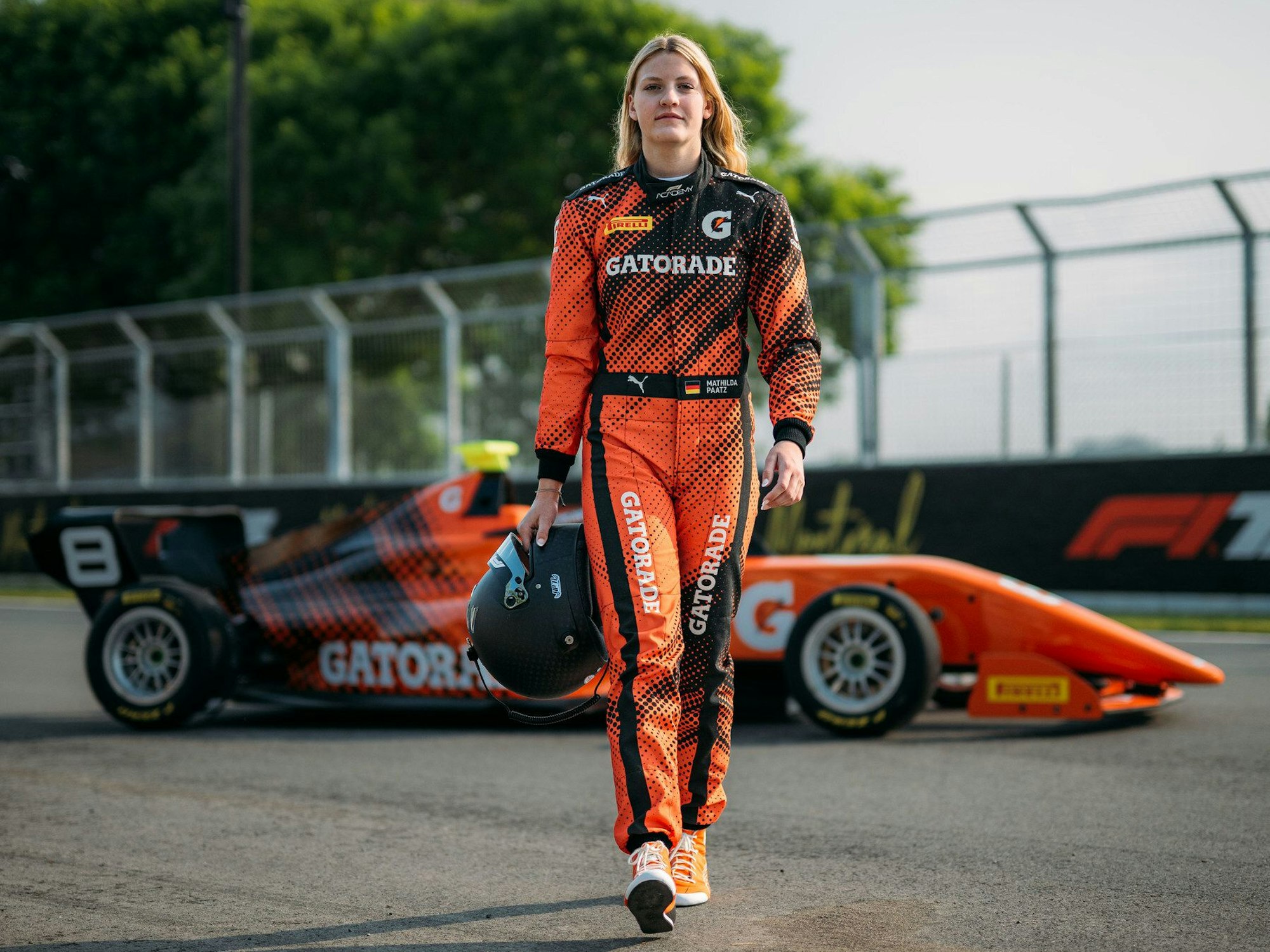 Mathilda Paatz vor ihrem Rennauto in orangener Fahrkleidung.