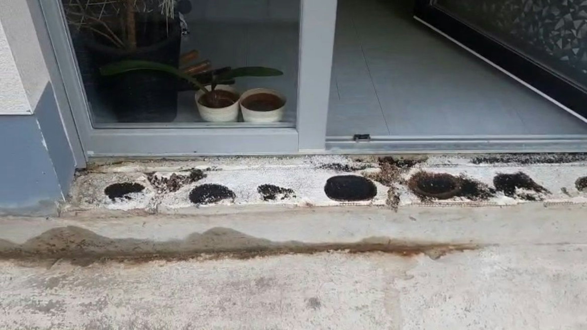 Vor einer Terrassentür fehlen Fliesen, im Boden sind Feuchtigkeitsflecken.