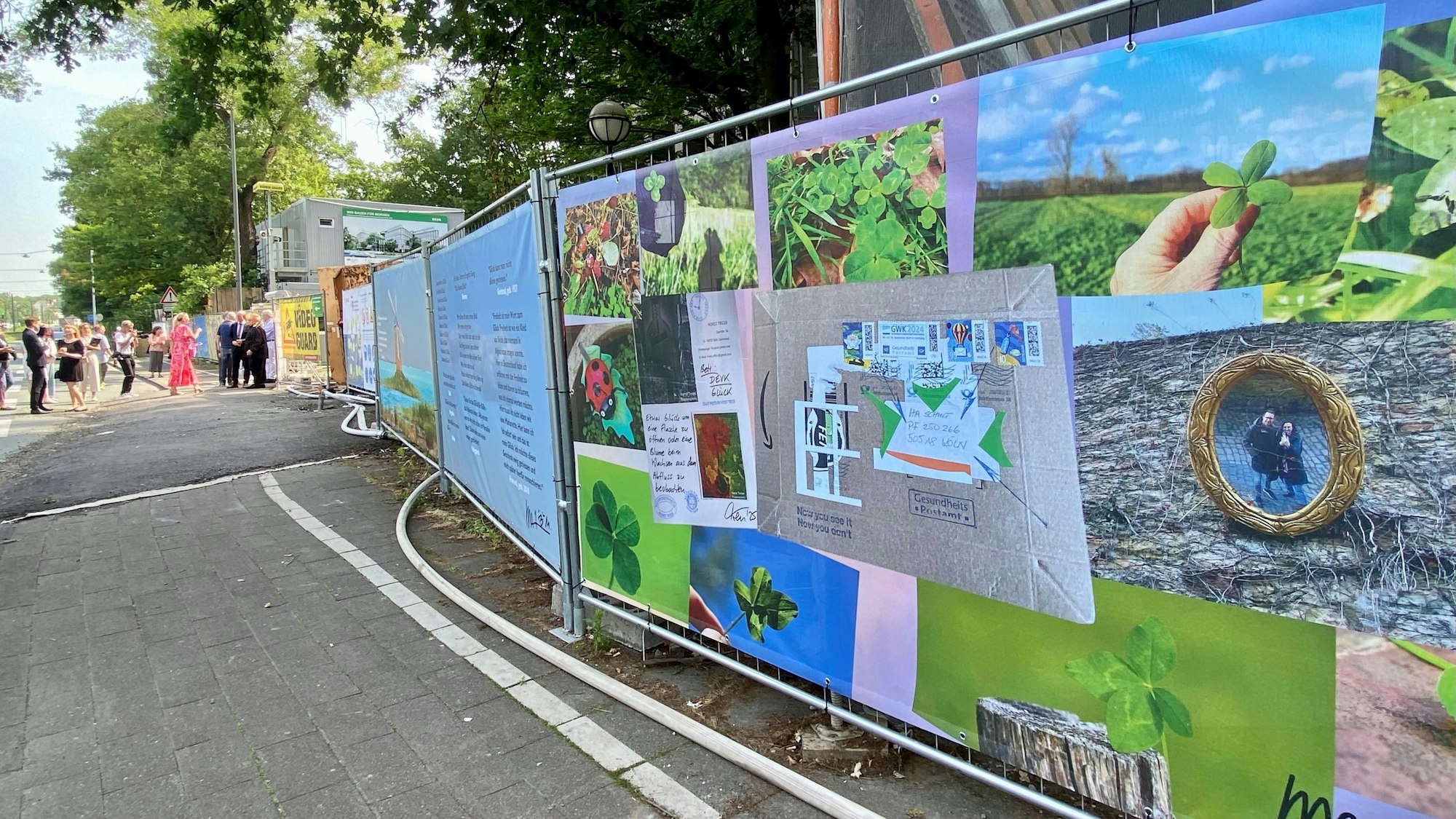 An einem Bauzaun hängen Bilder mit Kleeblättern.