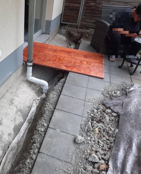 An einer Terrasse ist ein Graben ausgehoben worden, darüber liegt ein Holzbrett.