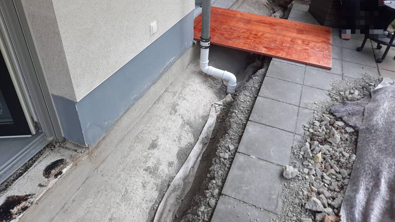 An einer Terrasse ist ein Graben ausgehoben worden, darüber liegt ein Holzbrett.