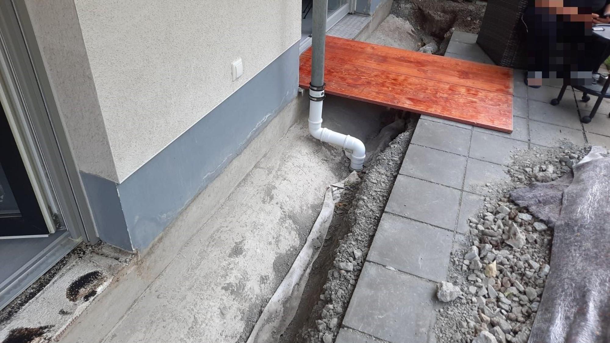 An einer Terrasse ist ein Graben ausgehoben worden, darüber liegt ein Holzbrett.