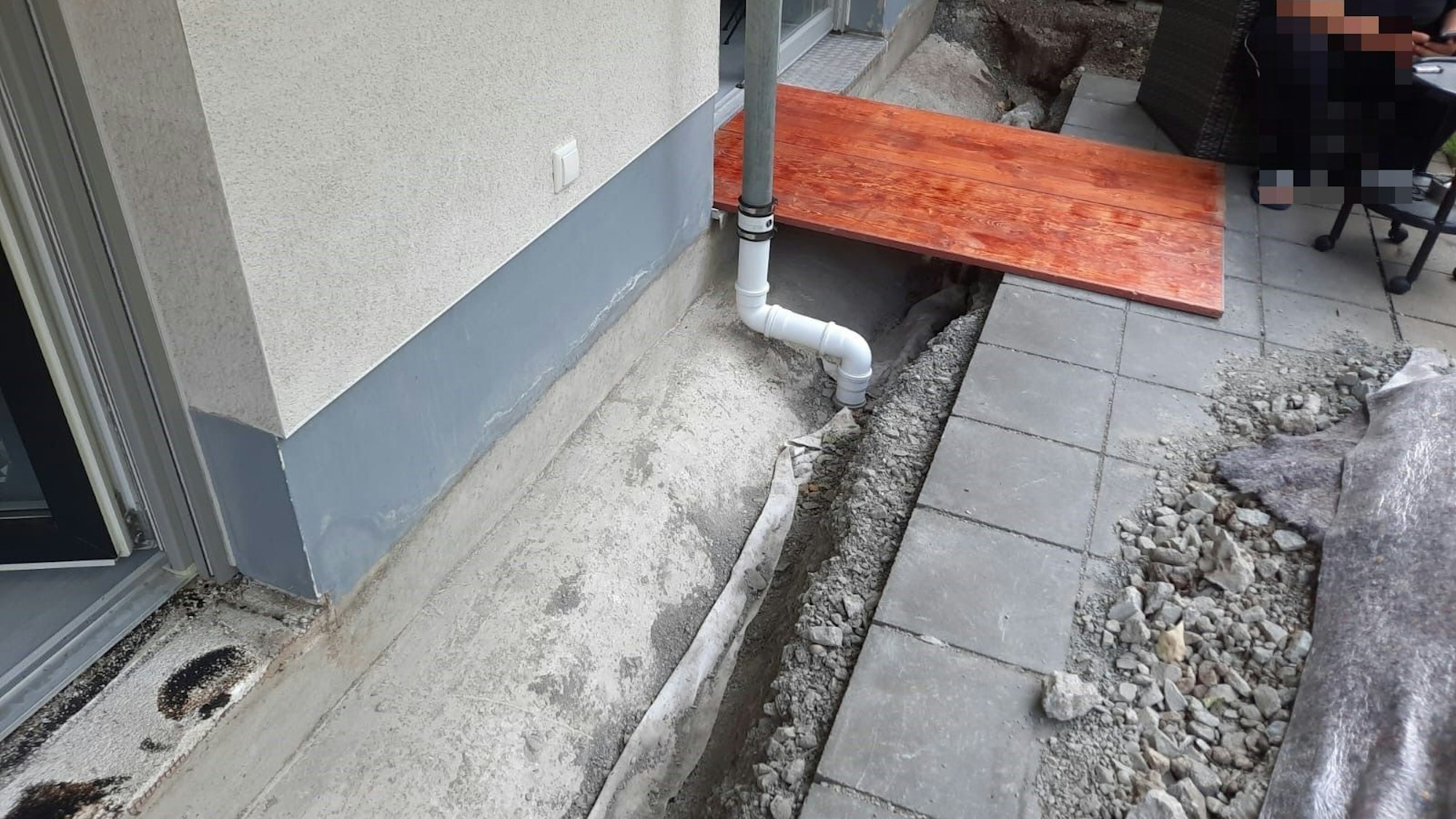 An einer Terrasse ist ein Graben ausgehoben worden, darüber liegt ein Holzbrett.