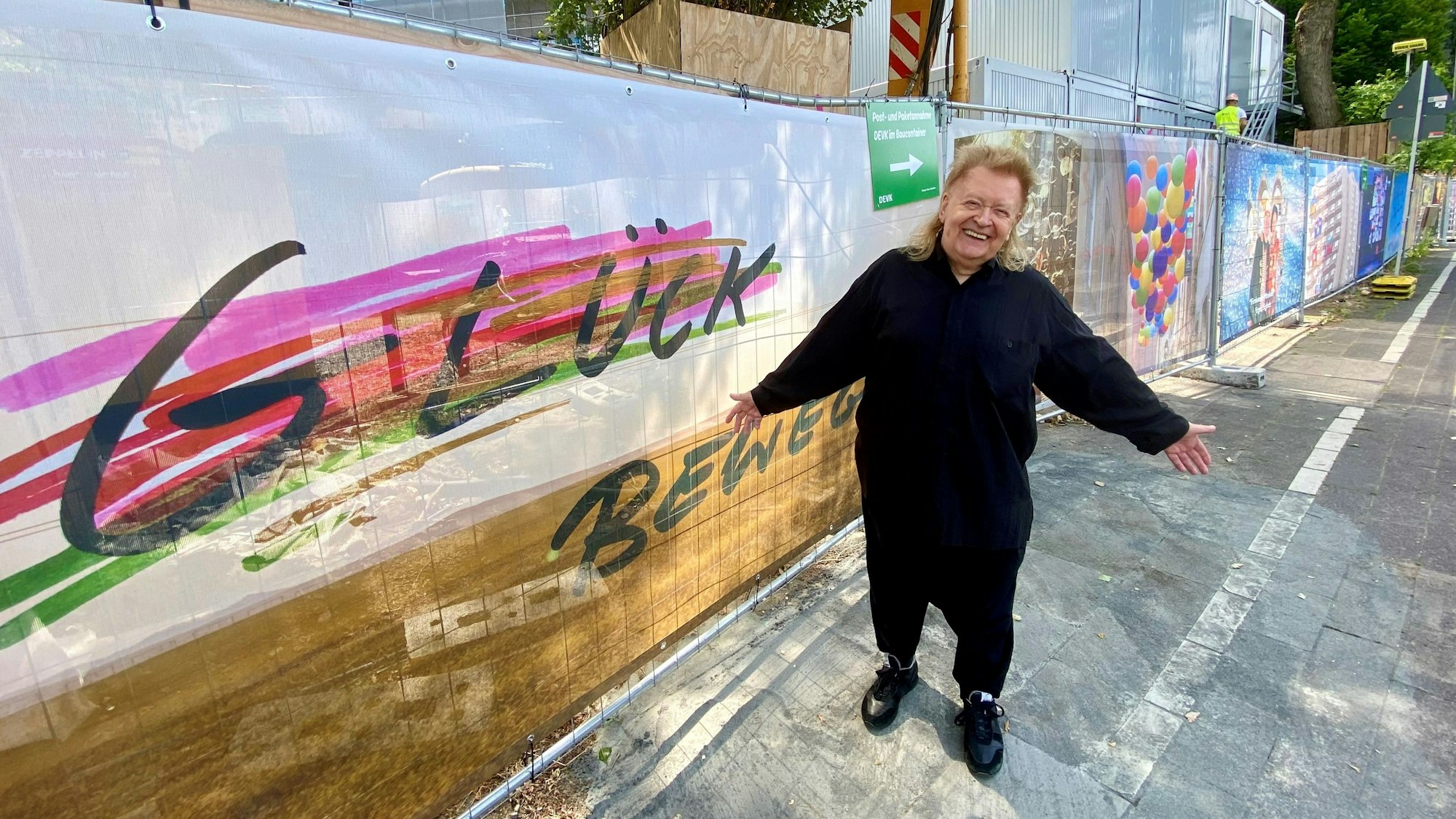 Ein Mann steht vor einem Zaun, auf dem „Glück“ geschrieben steht.