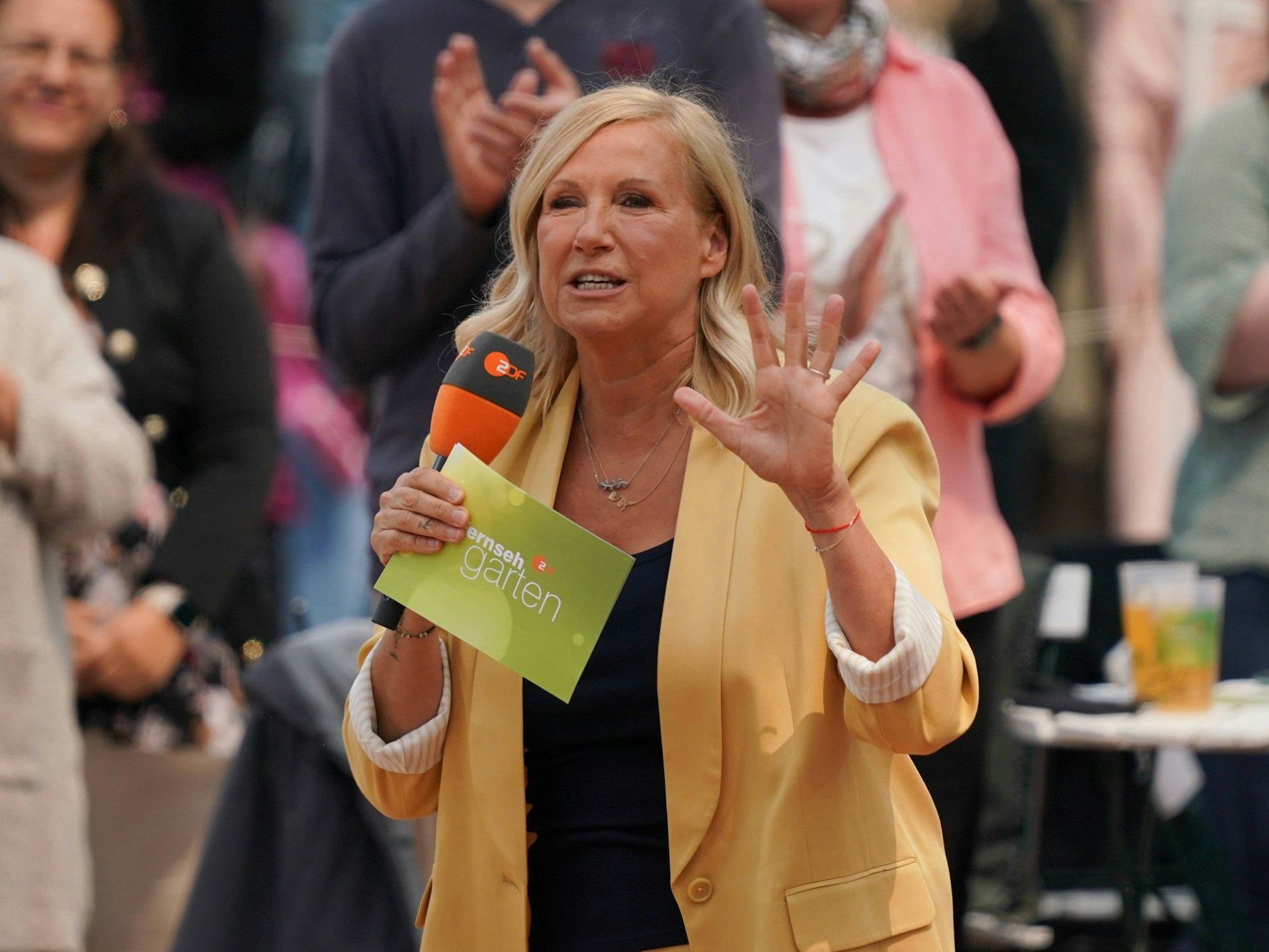 Andrea Kiewel bei der „Fernsehgarten“-Sendung am 8. Juni 2025 mit Mikrofon und Moderationskarten in den Händen.