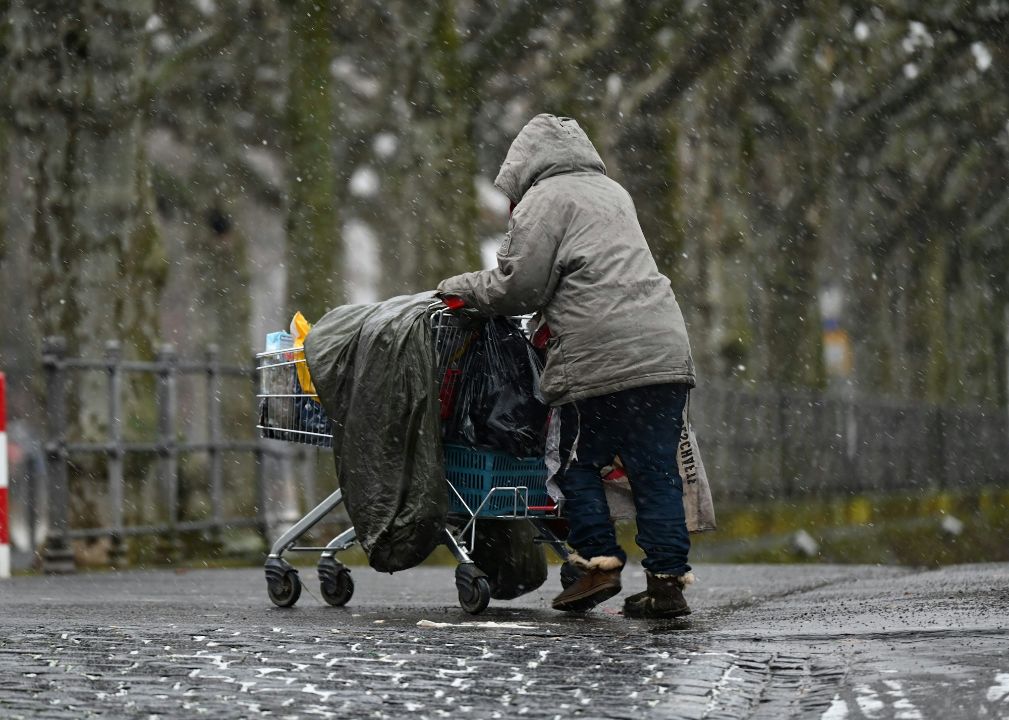 Eine obdachlose Frau schiebt ihr Hab und Gut in einem Einkaufswagen.