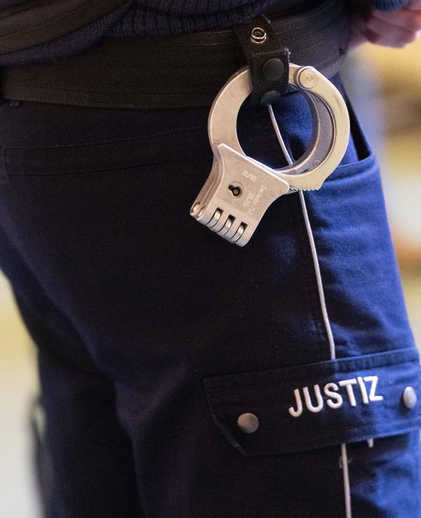 Ein Justizbeamter steht mit Handschellen im Verhandlungssaal eines Verwaltungsgerichts (Symbolfoto).