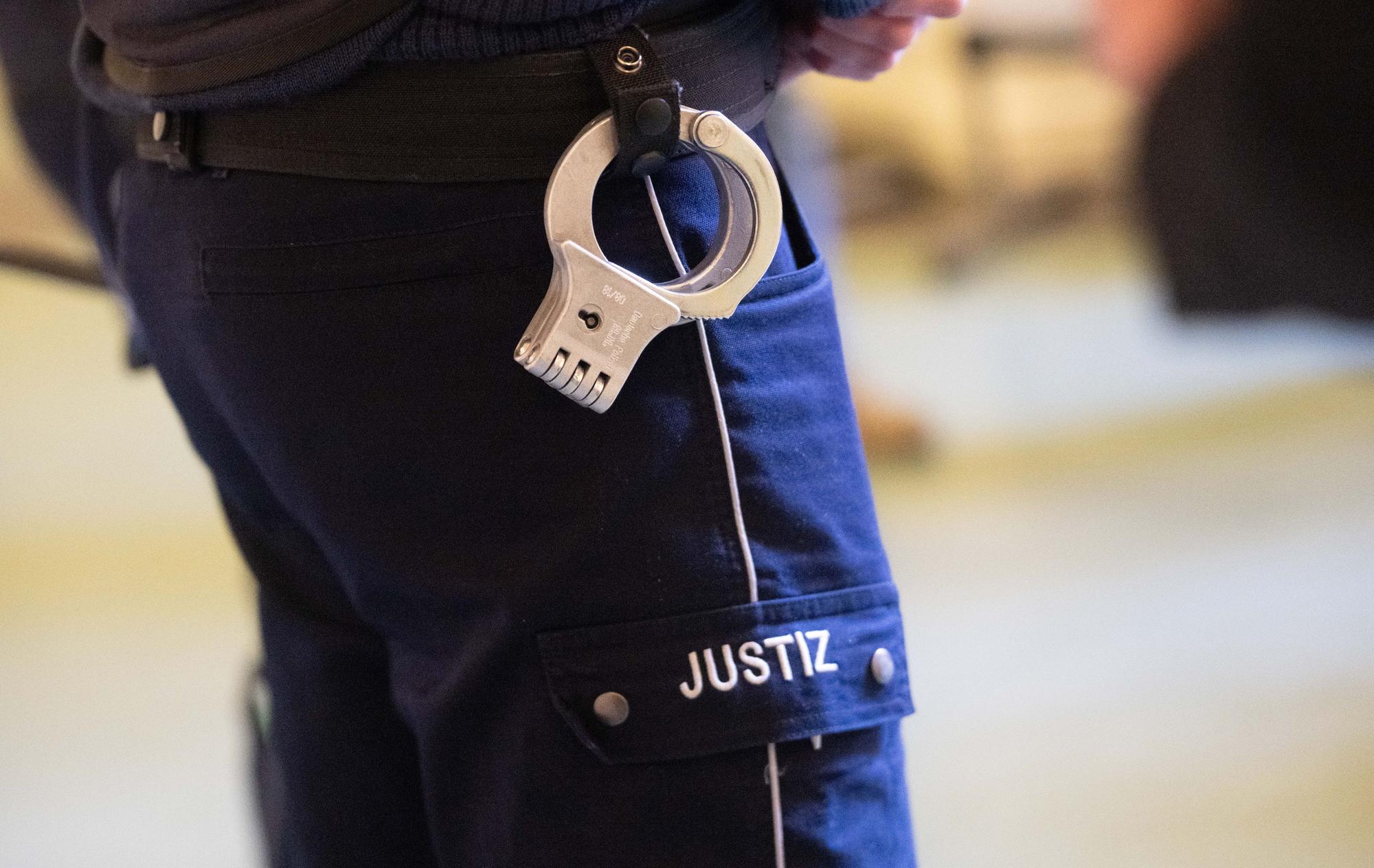 Ein Justizbeamter steht mit Handschellen im Verhandlungssaal eines Verwaltungsgerichts (Symbolfoto).