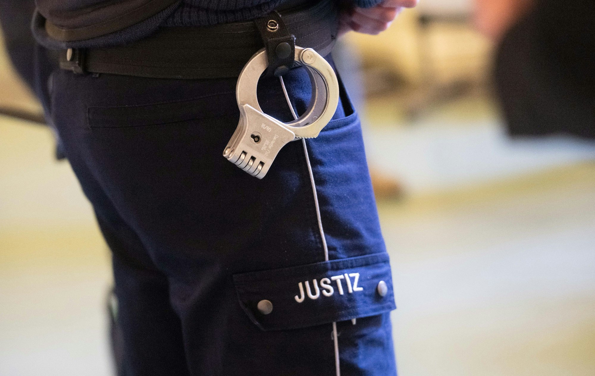 Ein Justizbeamter steht mit Handschellen im Verhandlungssaal eines Verwaltungsgerichts (Symbolfoto).