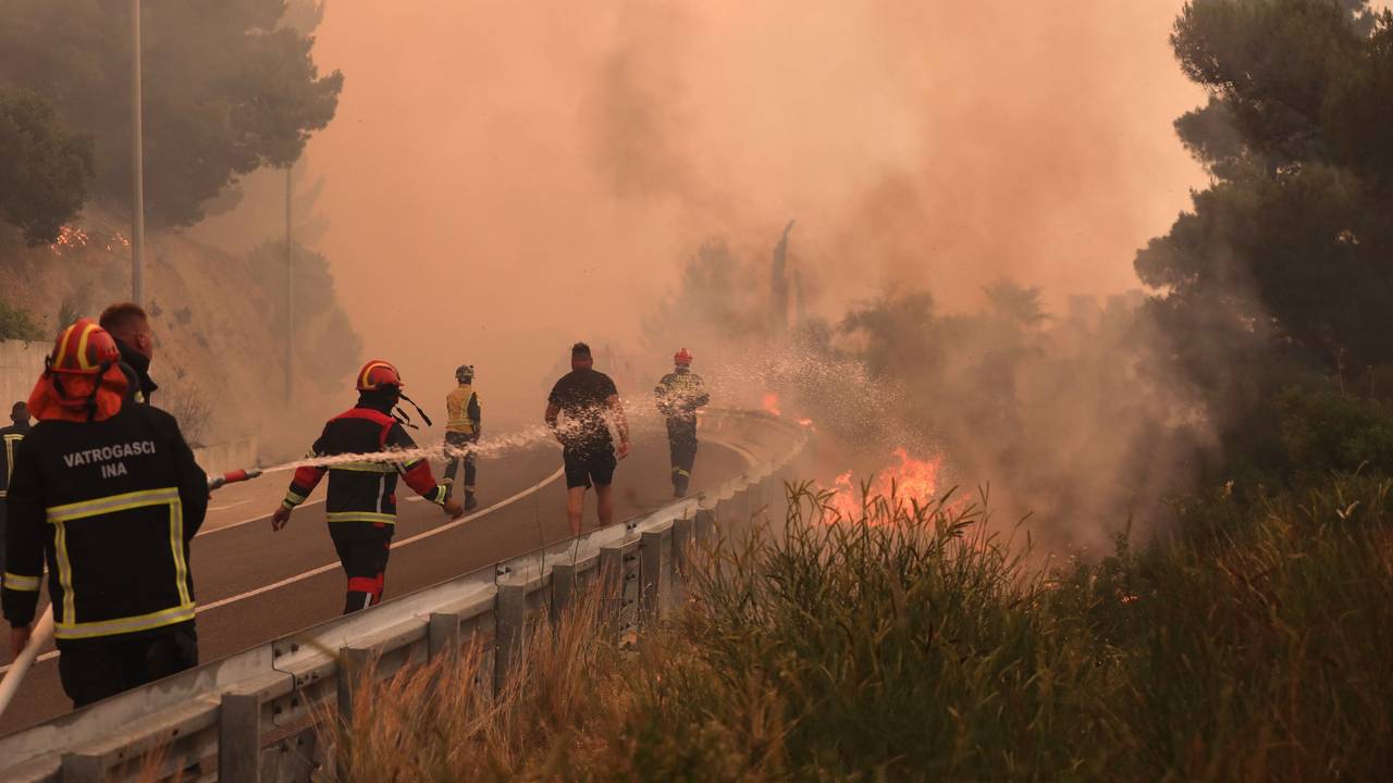 Feuerwehrleute löschen Brände neben einer Straße. Ein heftiger Vegetationsbrand wütet an der kroatischen Adria-Küste und führt dazu, dass viele Touristen fliehen.