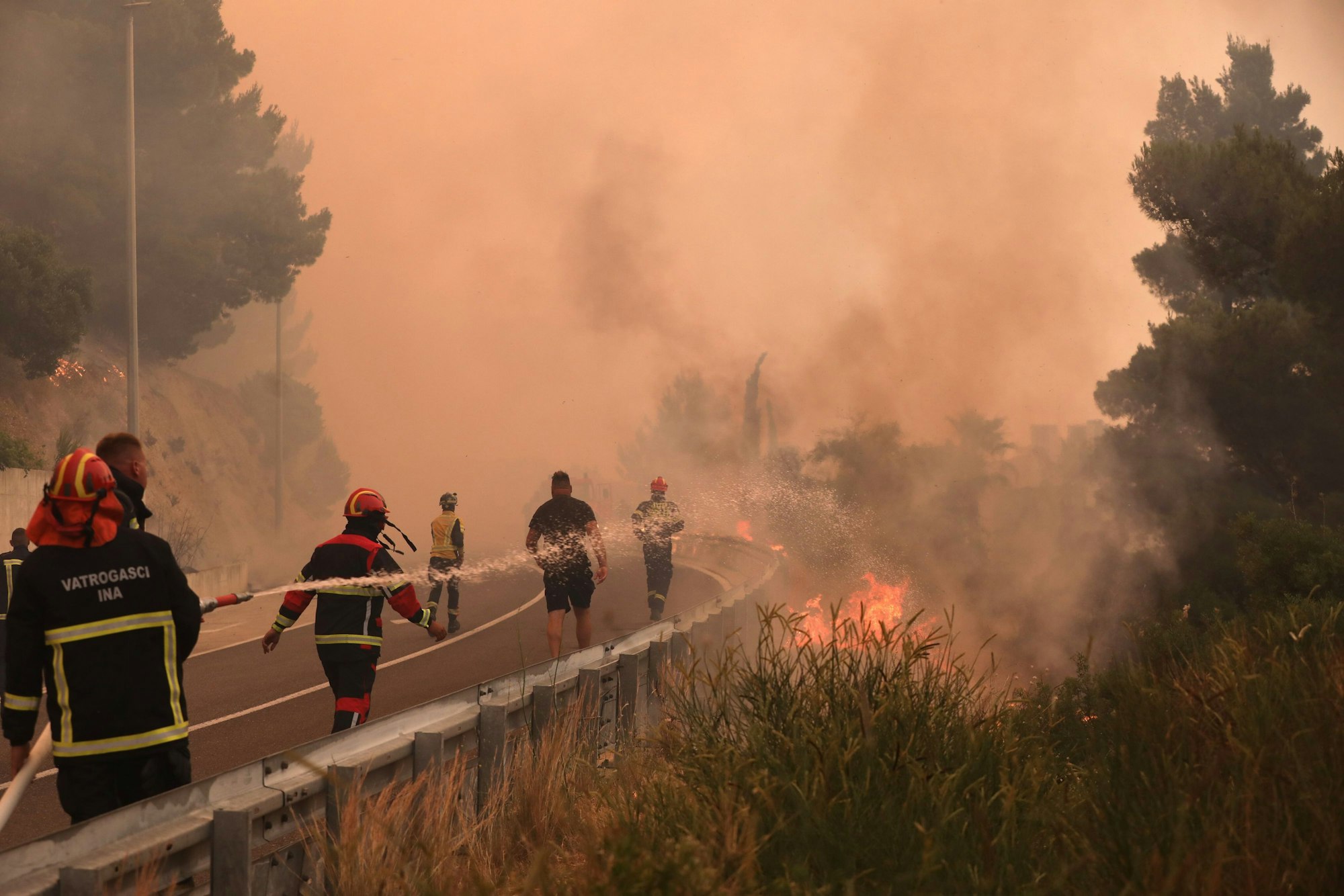 Feuerwehrleute löschen Brände neben einer Straße. Ein heftiger Vegetationsbrand wütet an der kroatischen Adria-Küste und führt dazu, dass viele Touristen fliehen.