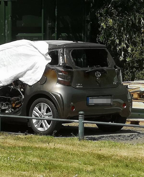 Eine ausgebranntes Auto ist in Düsseldorf mit einem Tuch abgedeckt. In dem brennenden Auto hatten Einsatzkräfte eine Leiche entdeckt.