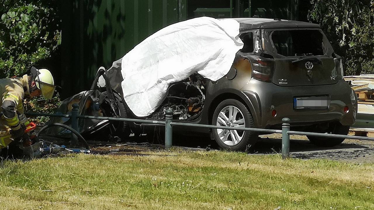 Eine ausgebranntes Auto ist in Düsseldorf mit einem Tuch abgedeckt. In dem brennenden Auto hatten Einsatzkräfte eine Leiche entdeckt.