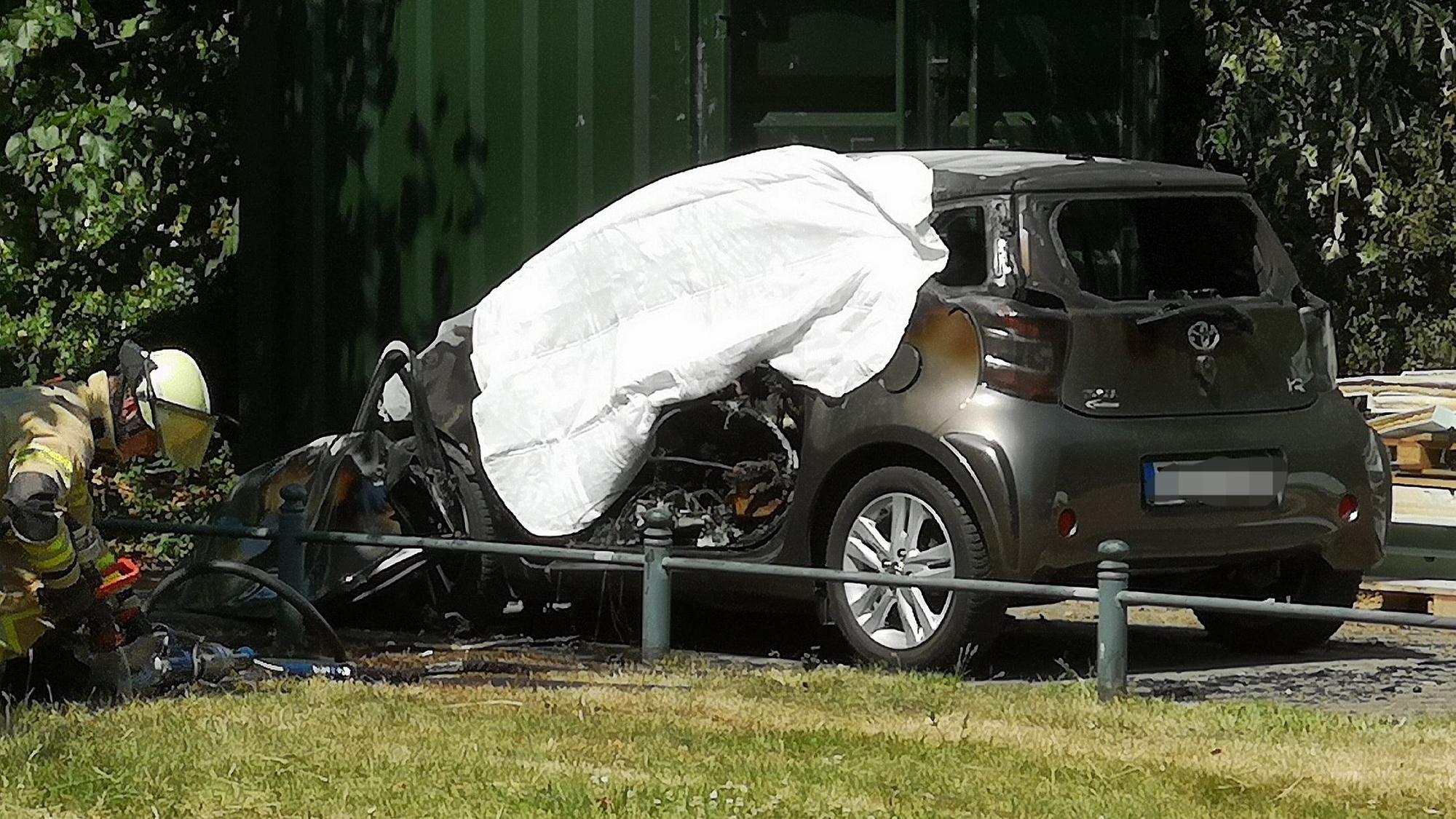 Eine ausgebranntes Auto ist in Düsseldorf mit einem Tuch abgedeckt. In dem brennenden Auto hatten Einsatzkräfte eine Leiche entdeckt.