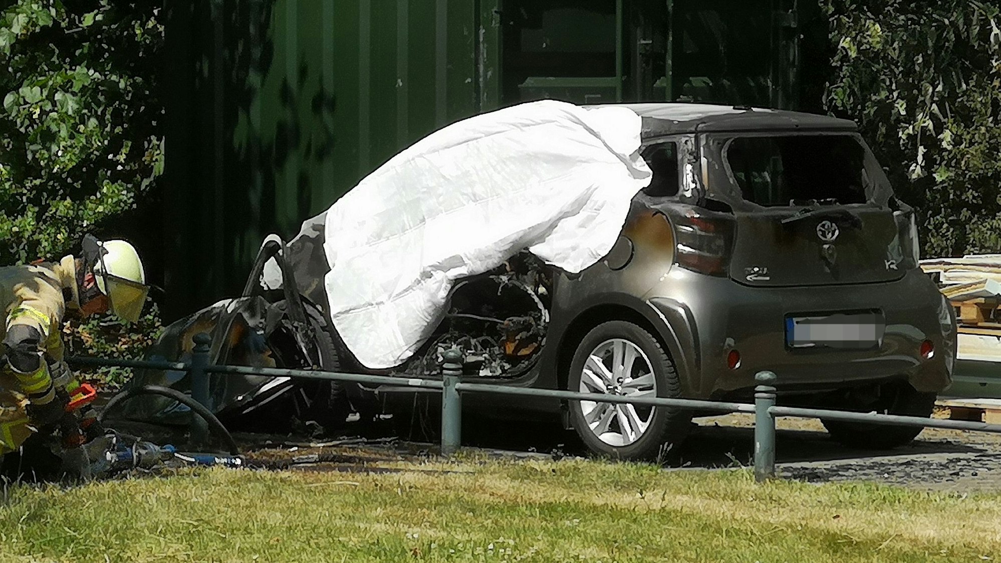 Eine ausgebranntes Auto ist in Düsseldorf mit einem Tuch abgedeckt. In dem brennenden Auto hatten Einsatzkräfte eine Leiche entdeckt.