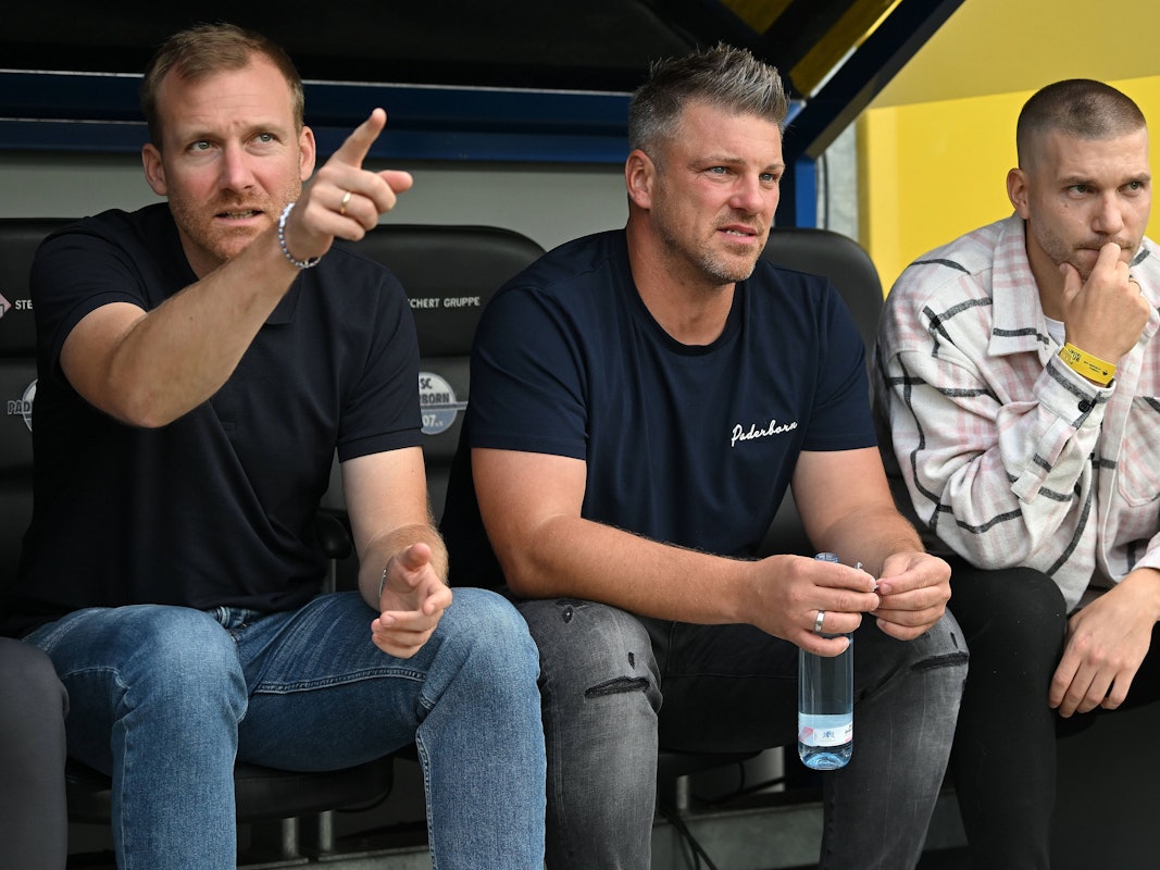 Lukas Kwasniok sitzt zwischen Benjamin Weber und Robert Leipertz auf der Paderborner Ersatzbank.