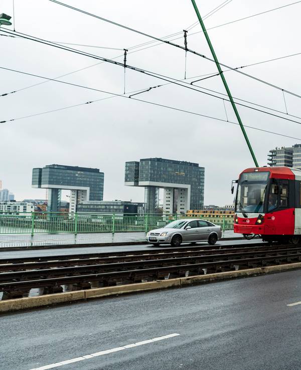 Eine Bahn fährt über eine Brücke, im Hintergrund die drei Kölner Kranhäuser.