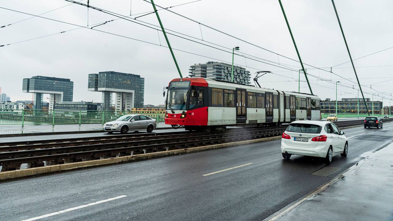 Eine Bahn fährt über eine Brücke, im Hintergrund die drei Kölner Kranhäuser.