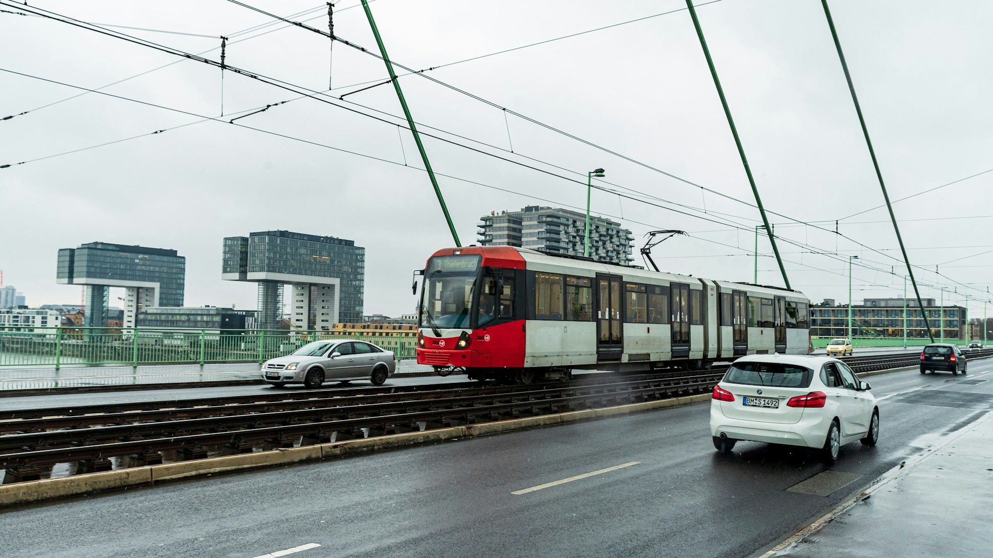 Eine Bahn fährt über eine Brücke, im Hintergrund die drei Kölner Kranhäuser.