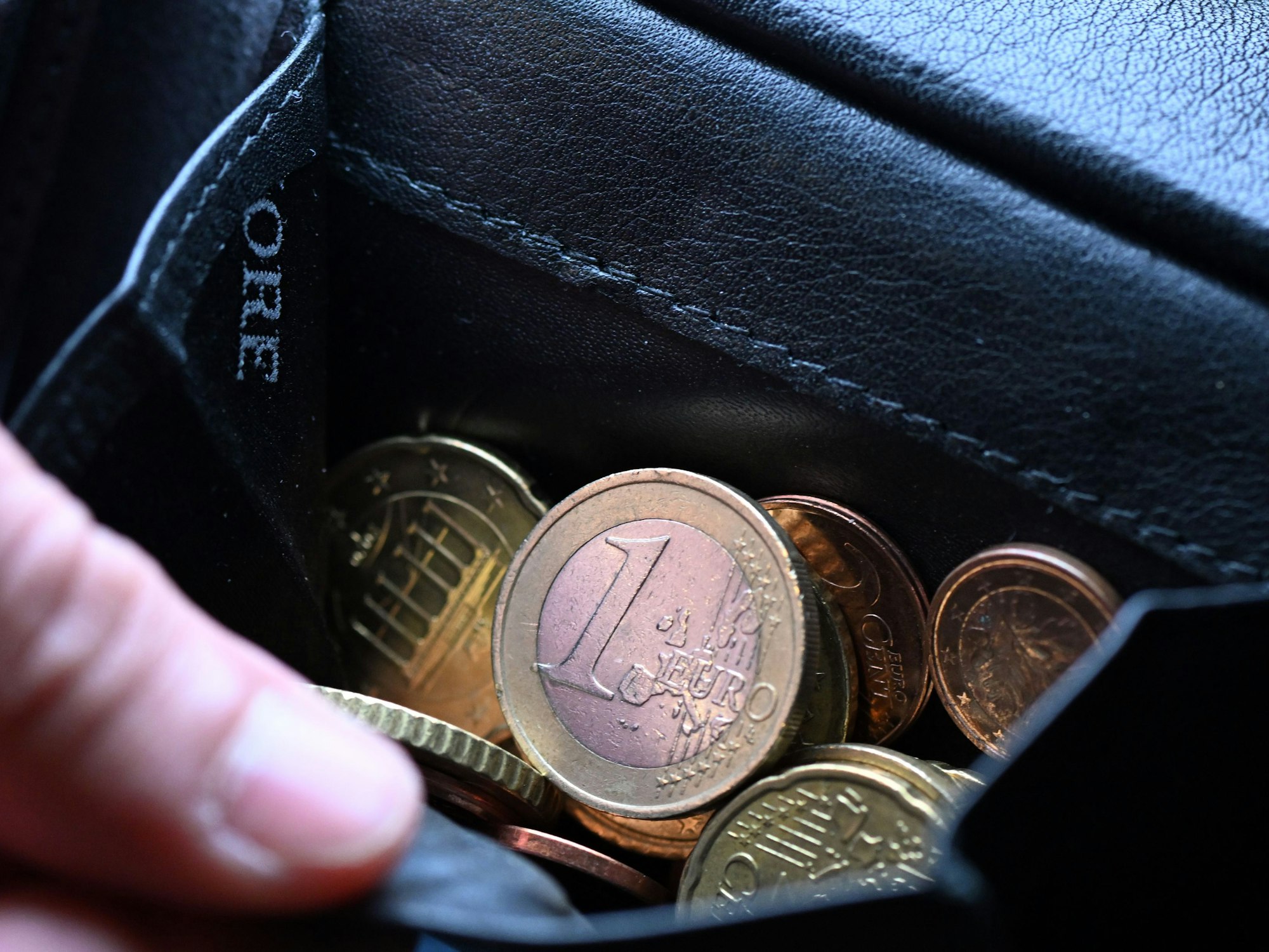Eine Hand greift in einen Geldbeutel mit Münzen (Symbolbild).