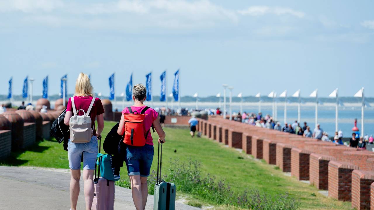 Zwei Frauen gehen bei sonnigem Wetter mit ihren Koffern über die Strandpromenade am Nordstrand der Insel Norderney.