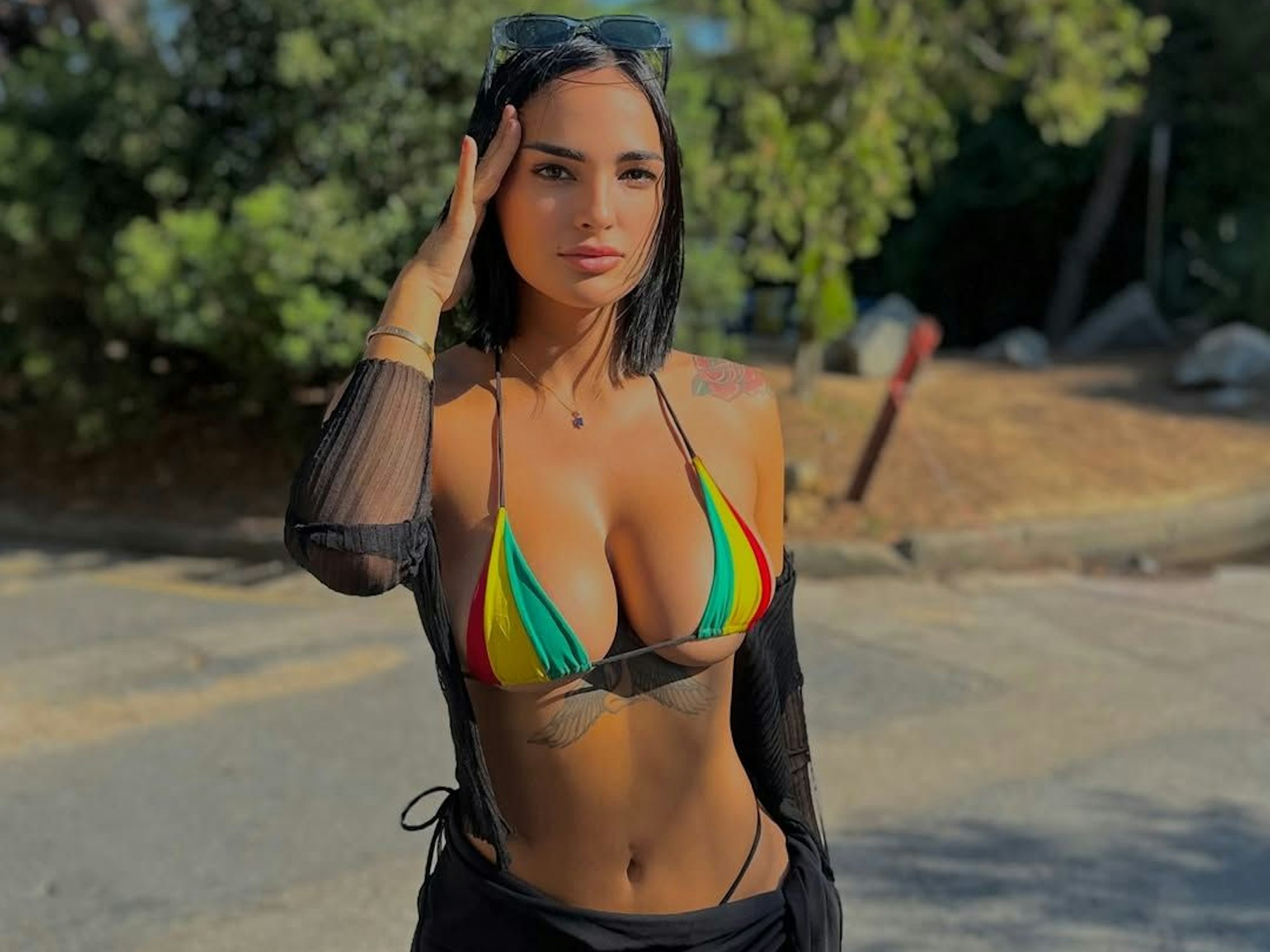 Claudia Bavel steht in einem bunten Bikini am Strand und fasst sich an den Kopf.