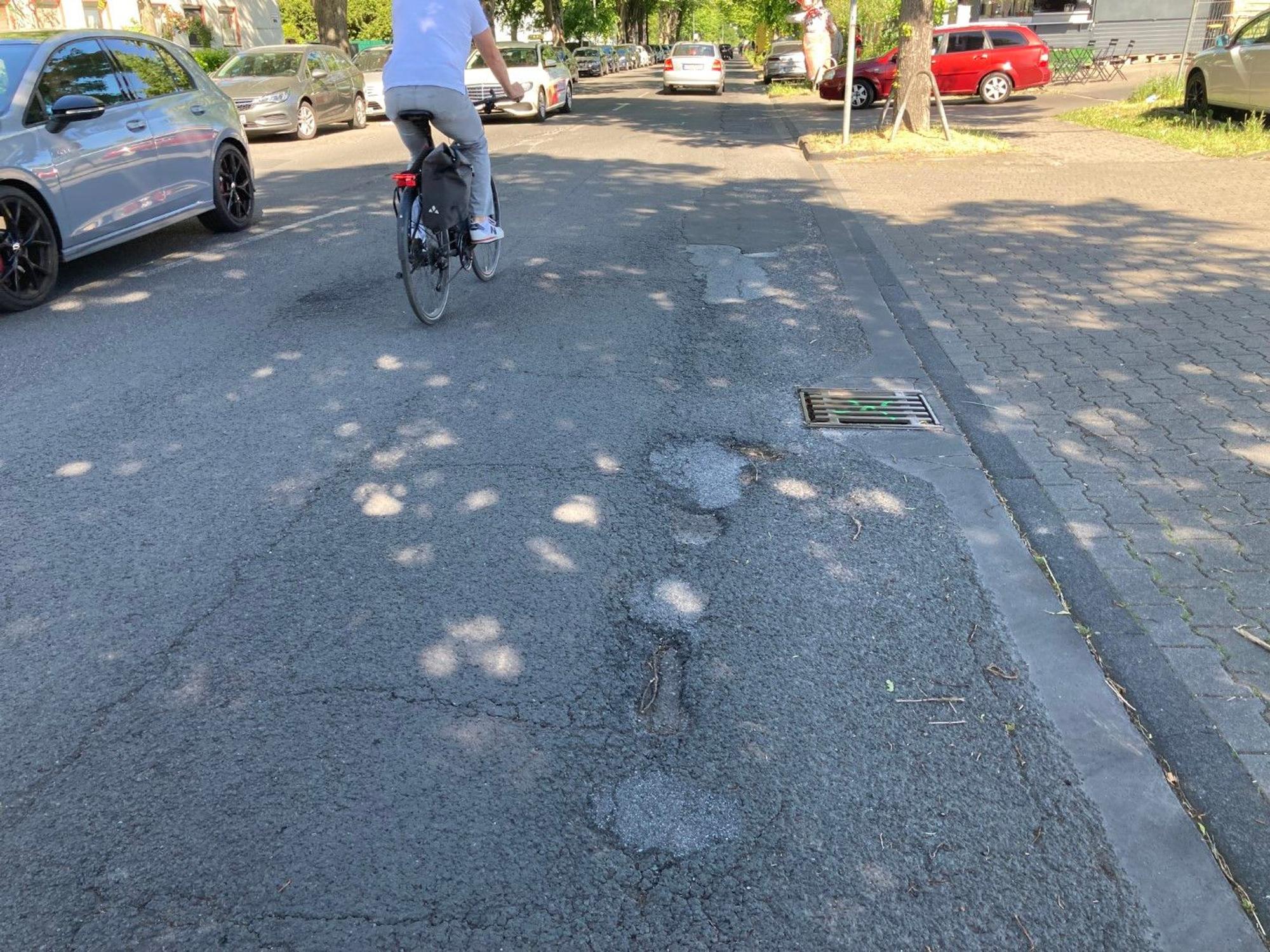 Ein Fahrradfahrer fährt über eine Straße mit Asphaltschäden.