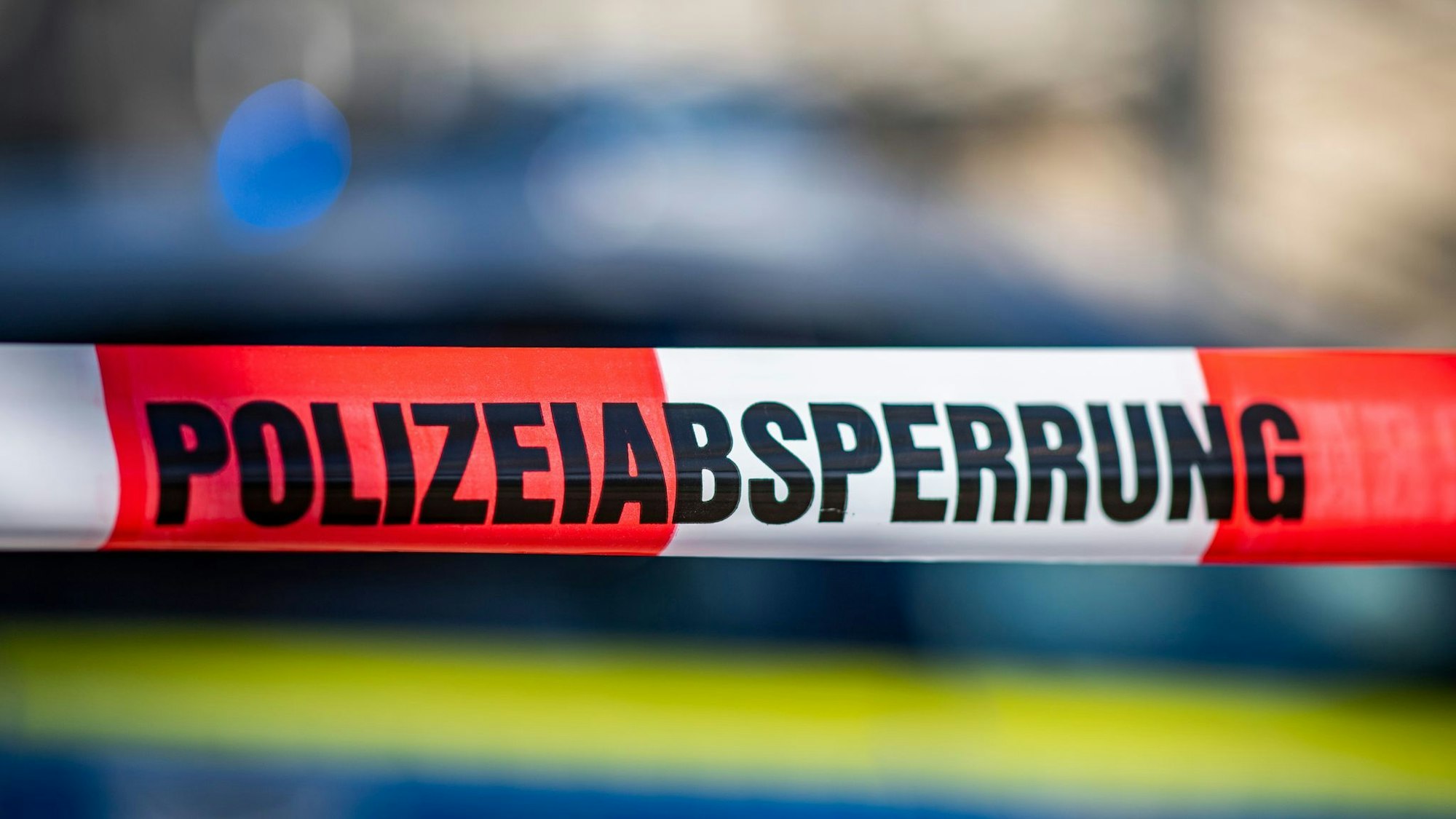 Ein Absperrband mit der Aufschrift „Polizeiabsperrung“ ist vor einem Polizeiwagen aufgespannt. (Symbolbild)