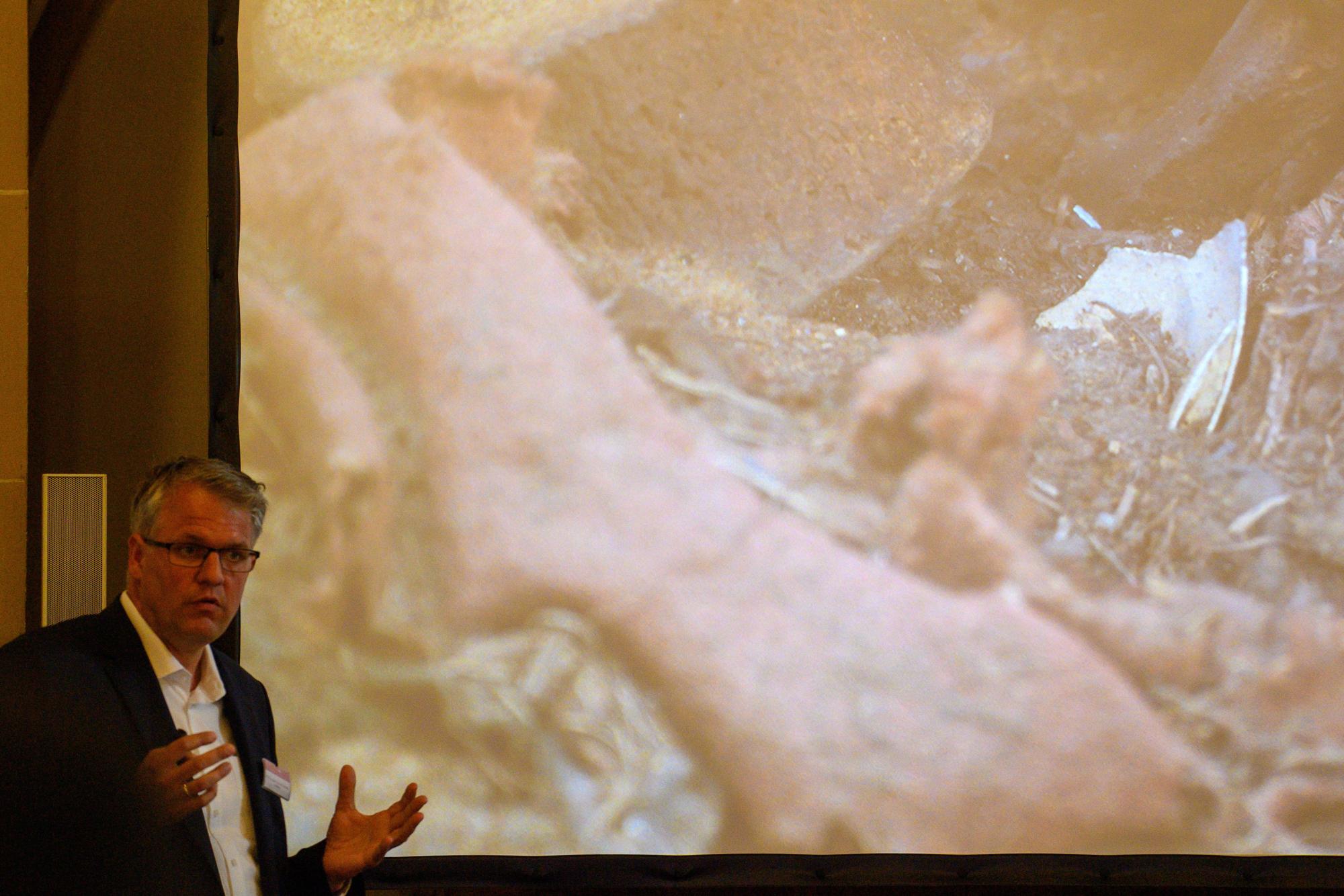 Donat Wehner (l) vom Landesamt für Denkmalpflege und Archäologie Sachsen-Anhalt erklärt in der Sakristei des Magdeburger Doms mit Hilfe einer Live-Videoübertragung aus dem Inneren der Einhausung, die das Grab von Otto dem Großen umgibt, das Inneren der Holzkiste im geöffneten Sarkophages, in dem Stoffreste und Eierschalen zu sehen sind.