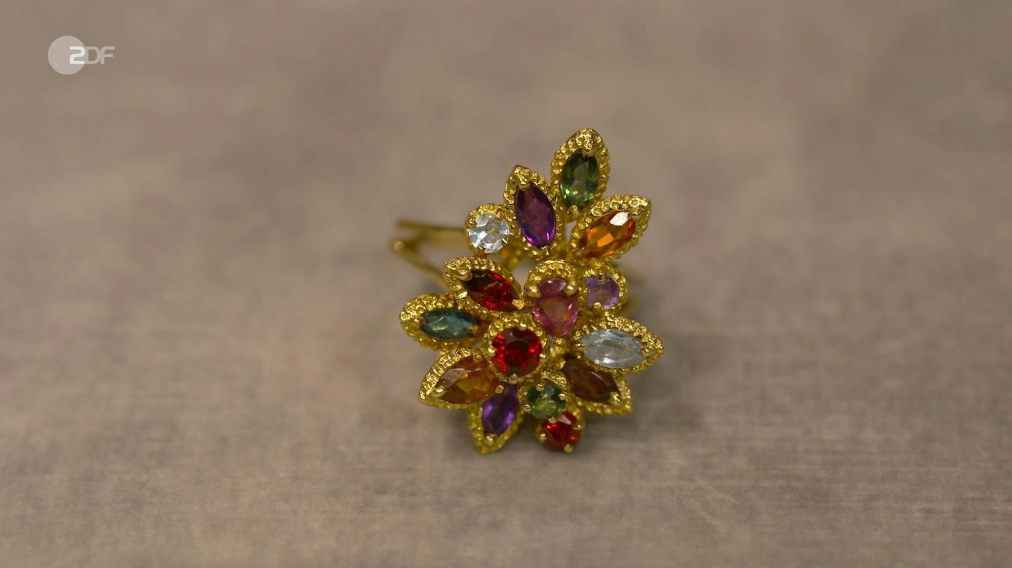 Wendela Horz verortete einen Ring aus 750er Gold mit bunten Edelsteine nach Indien. Der Wunschpreis lag bei 400 Euro. Die Expertin schätzte sogar 800 Euro, denn allein der Goldwert brachte schon 740 Euro. Händlerin Elisabeth Nüdling zahlte am Ende sogar 1.200 Euro für den „Gute-Laune-Ring“ aus den 1980er Jahren.
(Bild: ZDF)