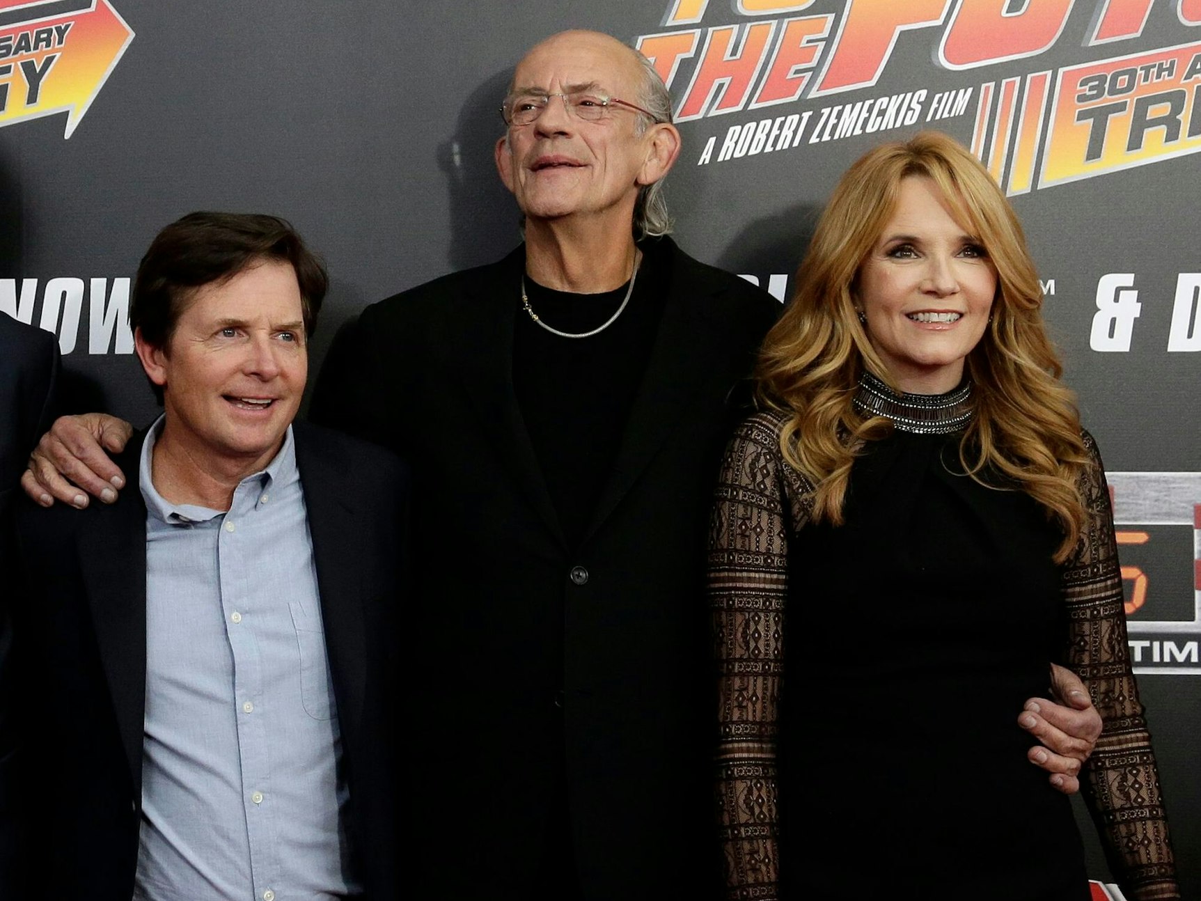 Drei Personen stehen vor einer Werbewand und lächeln in die Kamera.