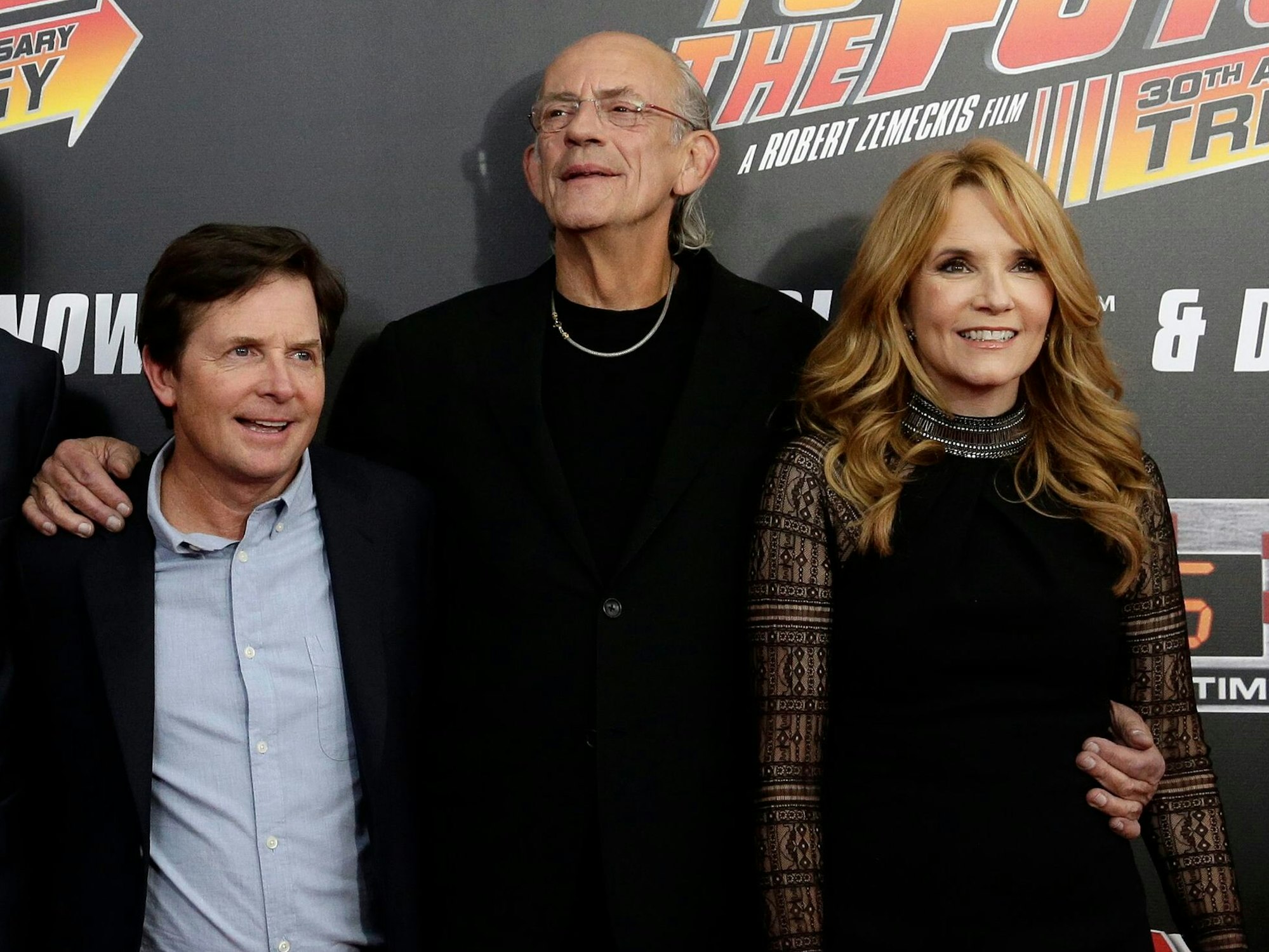 Drei Personen stehen vor einer Werbewand und lächeln in die Kamera.