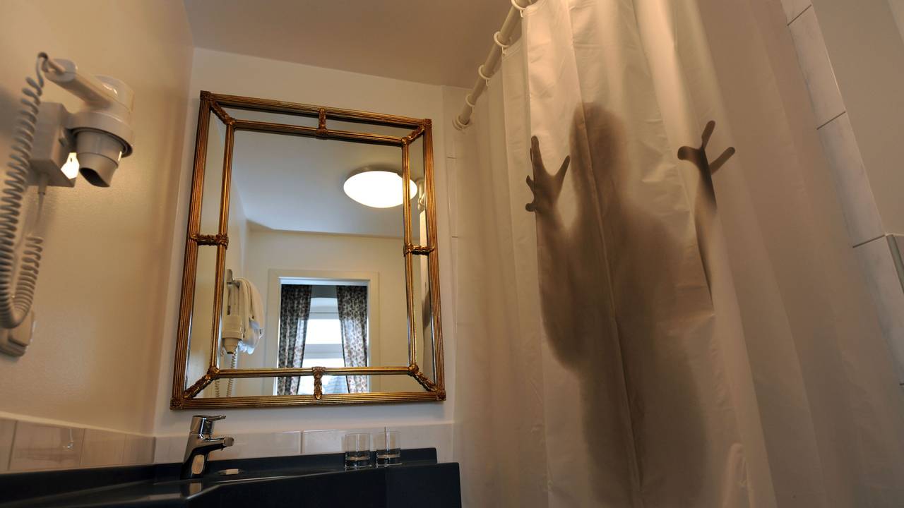 Die Silhouette eines Menschen hinter einem halbtransparenten Duschvorhang.
