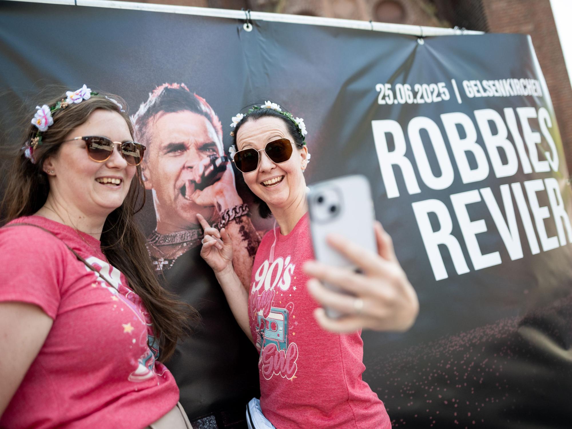 Sandra und Nicole stehen vor einem Poster, auf dem Robbie Williams zu sehen ist.