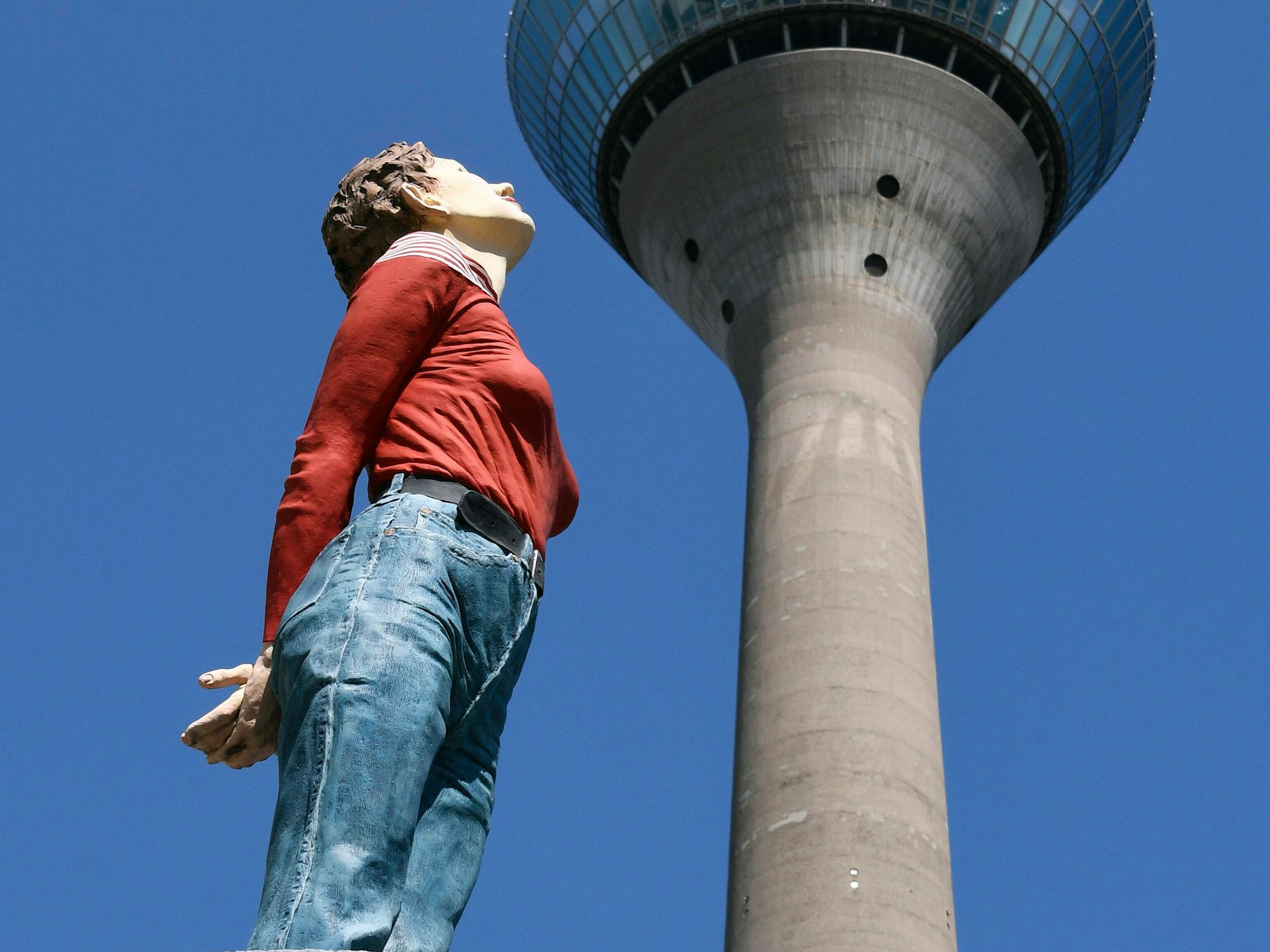 Die Skulptur aus der Serie Säulenheilige des deutschen Künstlers Christoph Pöggeler. Marlies blickt hoch auf den Düsseldorfer Rheinturm.