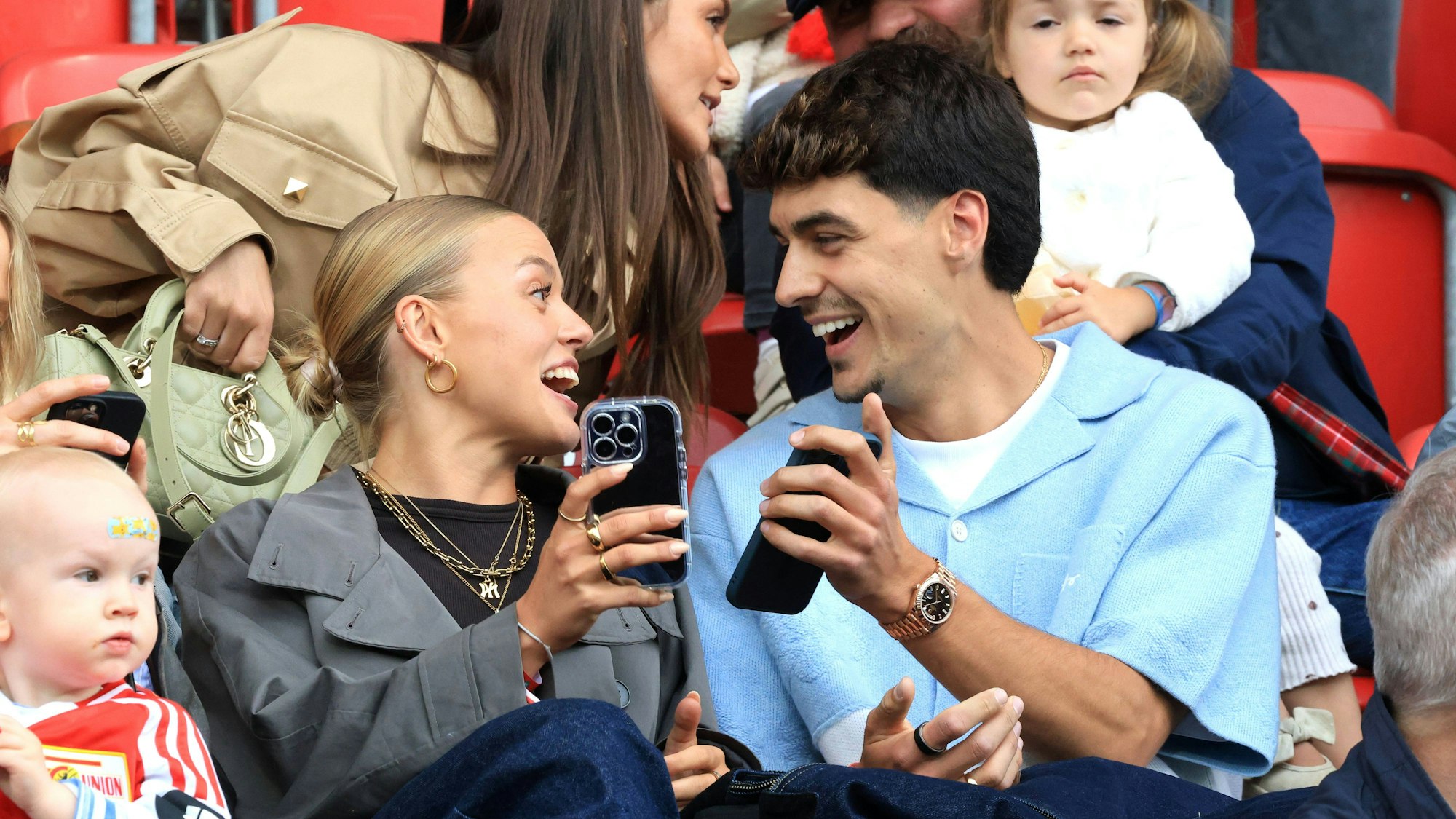 Diogo Leite sitzt neben seiner Partnerin auf der Tribüne und zeigt ihr etwas auf dem Handy.