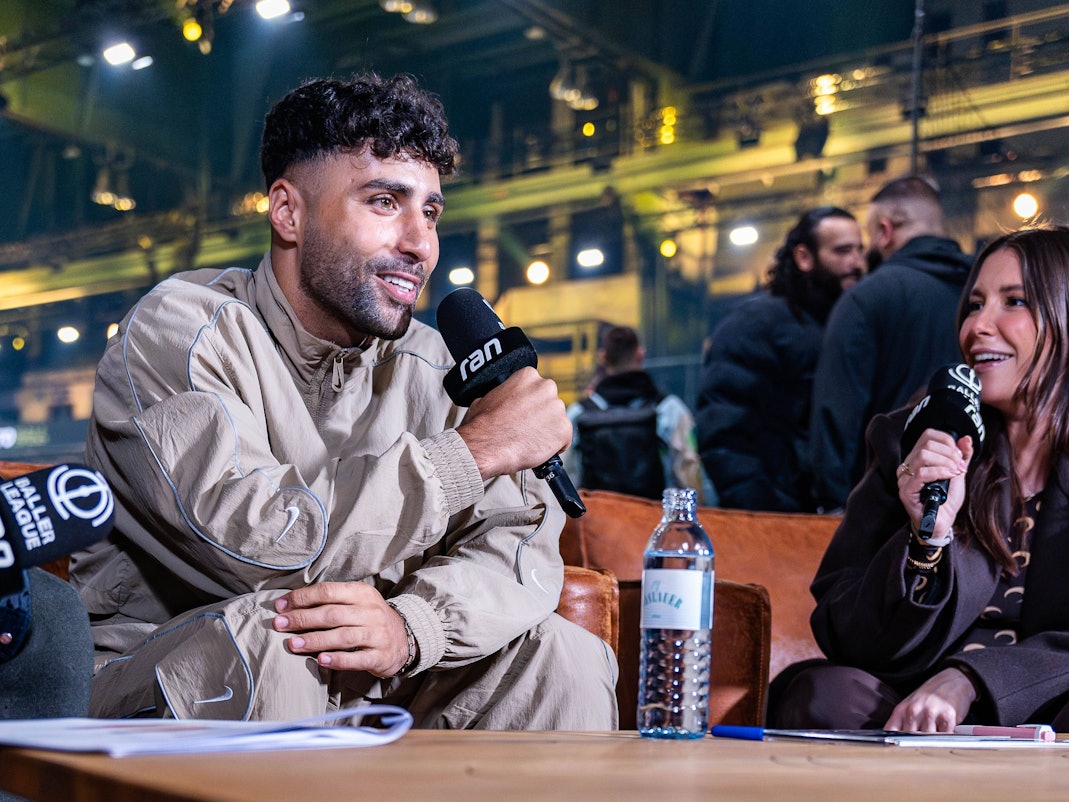 Nader El-Jindaoui sitzt mit Mikrofon auf der Couch bei der Baller League.