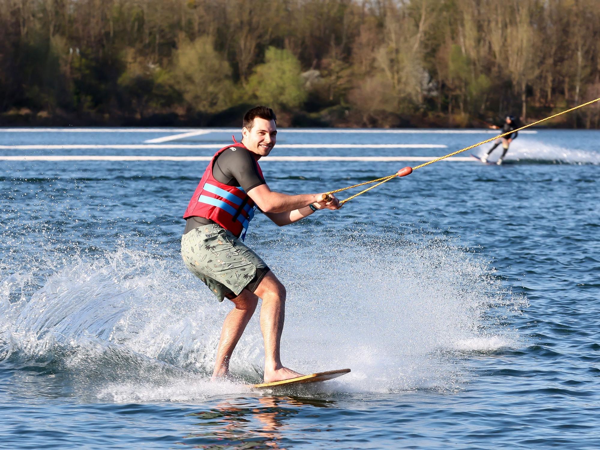Ein Mann fährt Wakeboard auf einem See und lacht