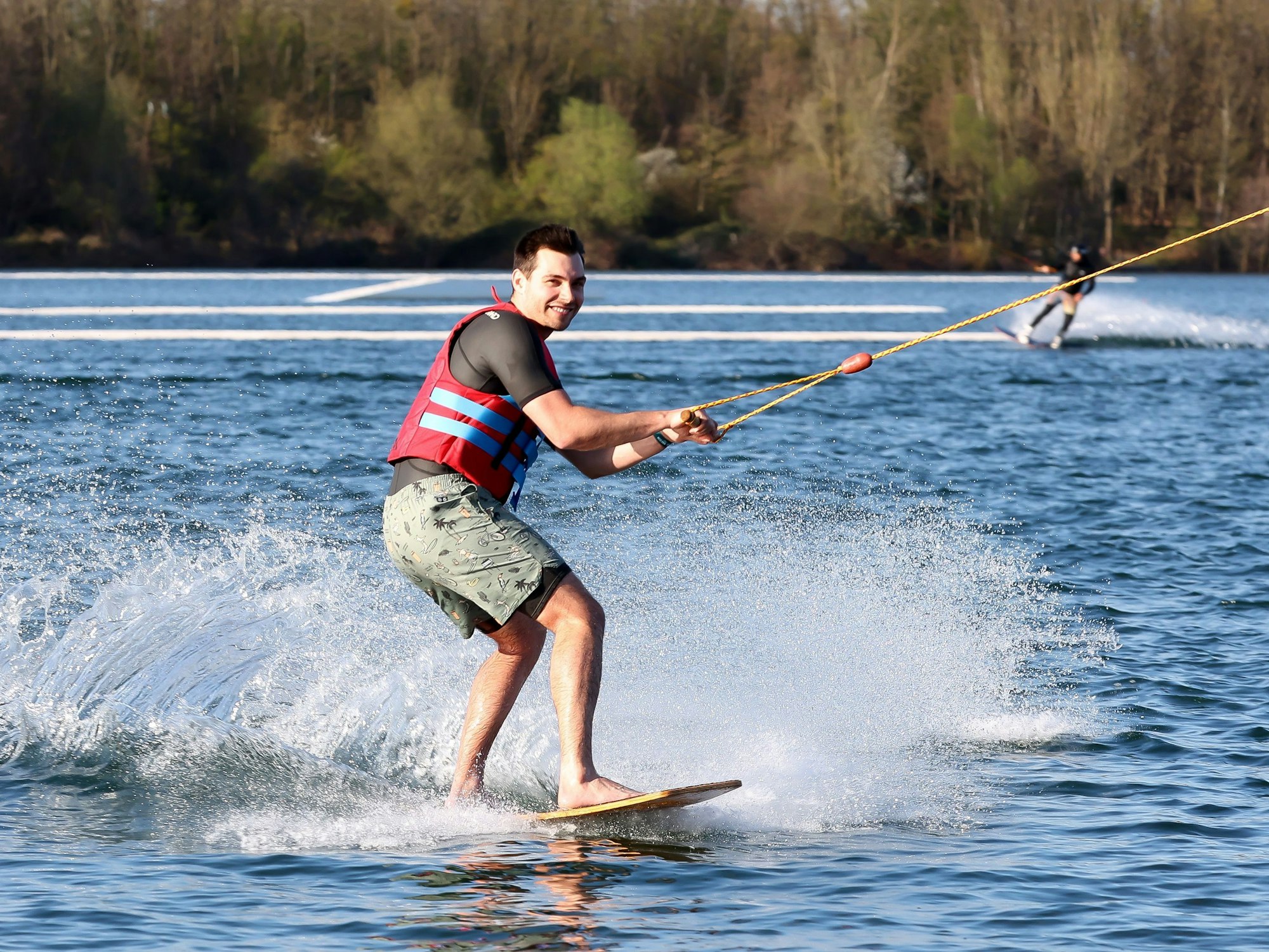 Ein Mann fährt Wakeboard auf einem See und lacht