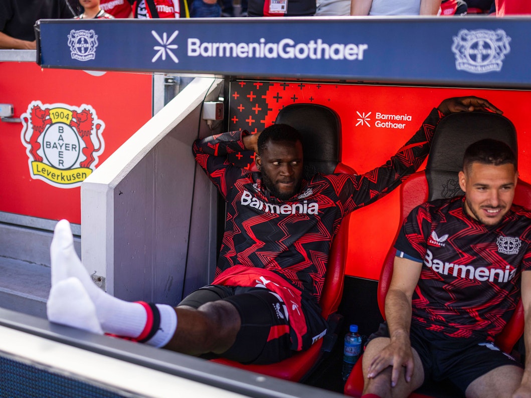 Victor Boniface sitzt auf der Bank und streckt seine Beine aus.