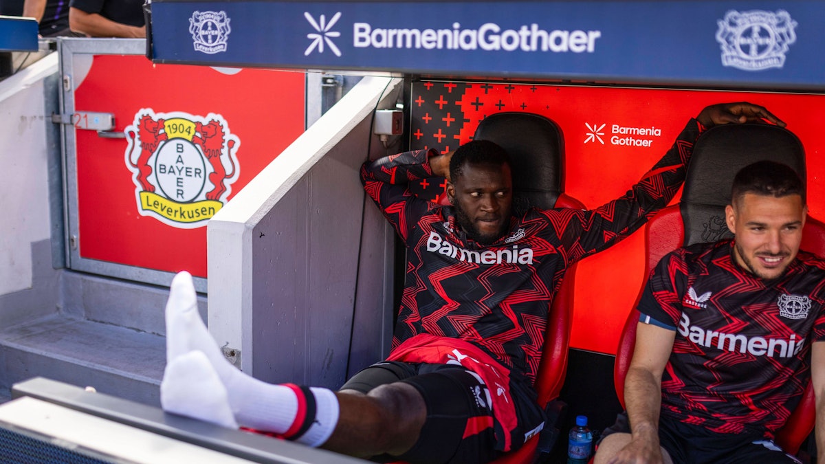 Victor Boniface sitzt auf der Bank und streckt seine Beine aus.