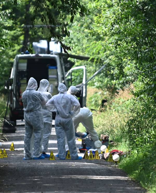 Ermittler stehen auf einem Weg. Polizisten haben nach einem Hinweis von Passanten an einem Waldweg eine tote Frau und ein totes Kleinkind entdeckt.